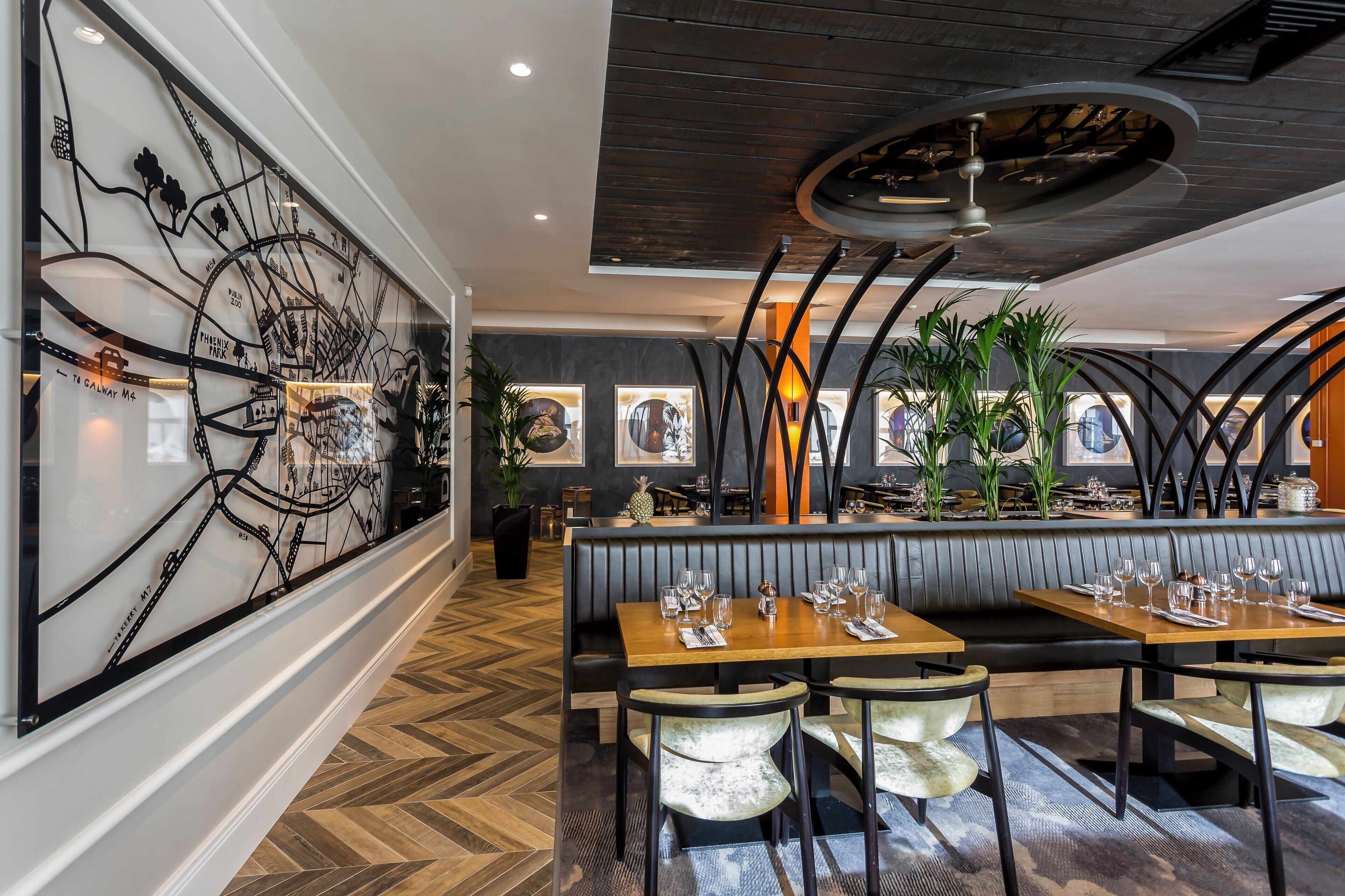 A restaurant with a modern interior, featuring a large wall art piece, wooden tables, and a herringbone floor pattern.