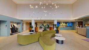 Un hall espacioso con un sofá seccional verde, diversas opciones de asiento, un mostrador de recepción y una lámpara de araña moderna.