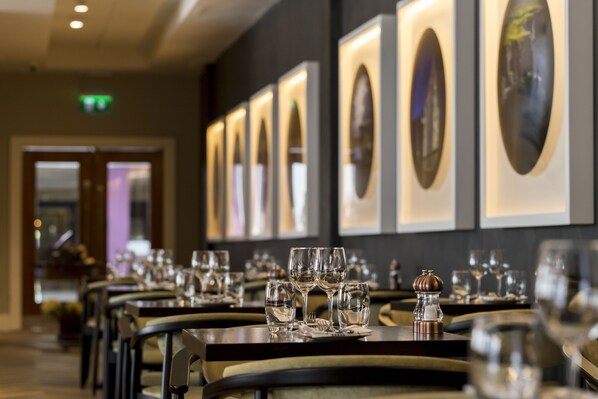 A restaurant with tables set for dining, framed artwork on the wall, and a door in the background.