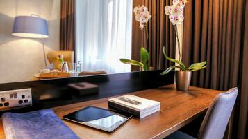 Habitación de hotel con un escritorio de madera, una tableta, un cuaderno, un bolígrafo y una orquídea en maceta.