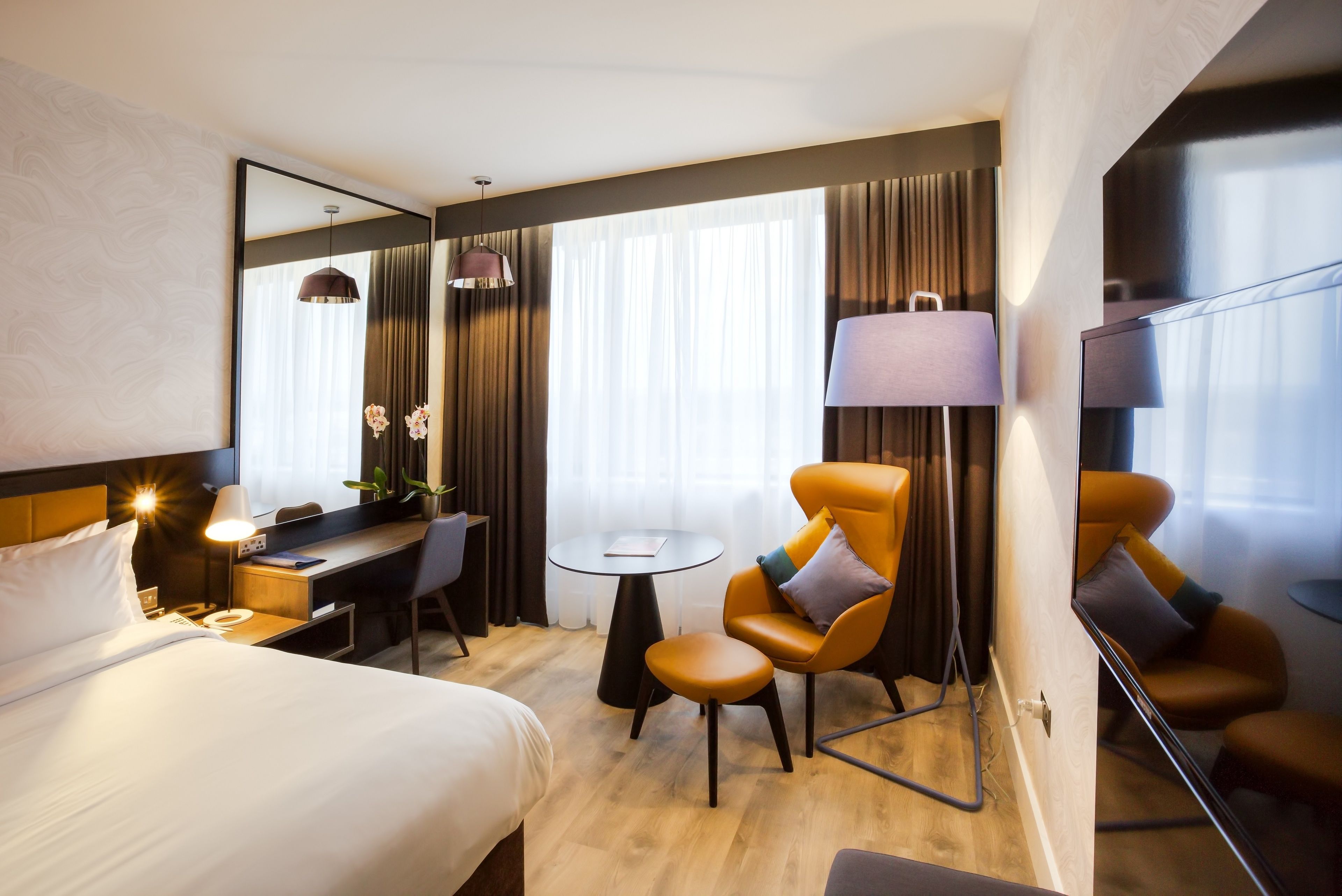 Ein Hotelzimmer mit einem Bett, einem Schreibtisch, zwei Stühlen, einer Lampe und einem Fernseher.