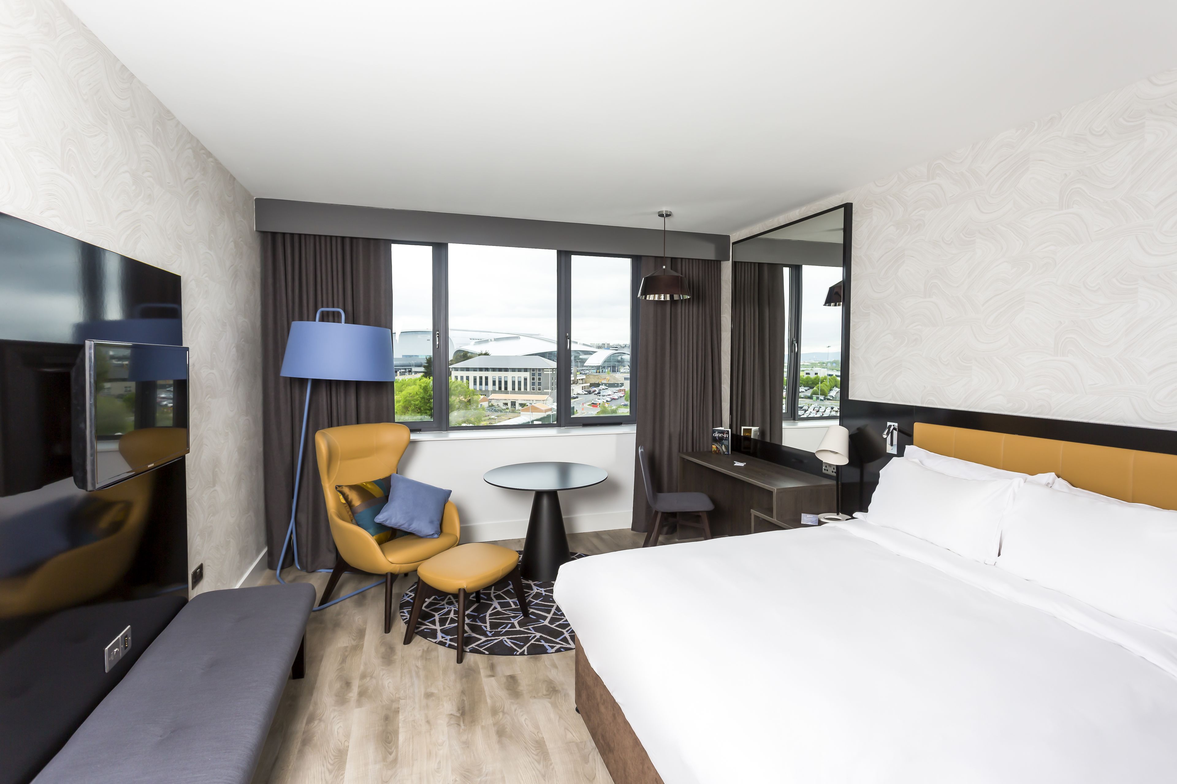 Une chambre d’hôtel avec un lit, un bureau, une chaise, une télévision et une vue sur la ville.