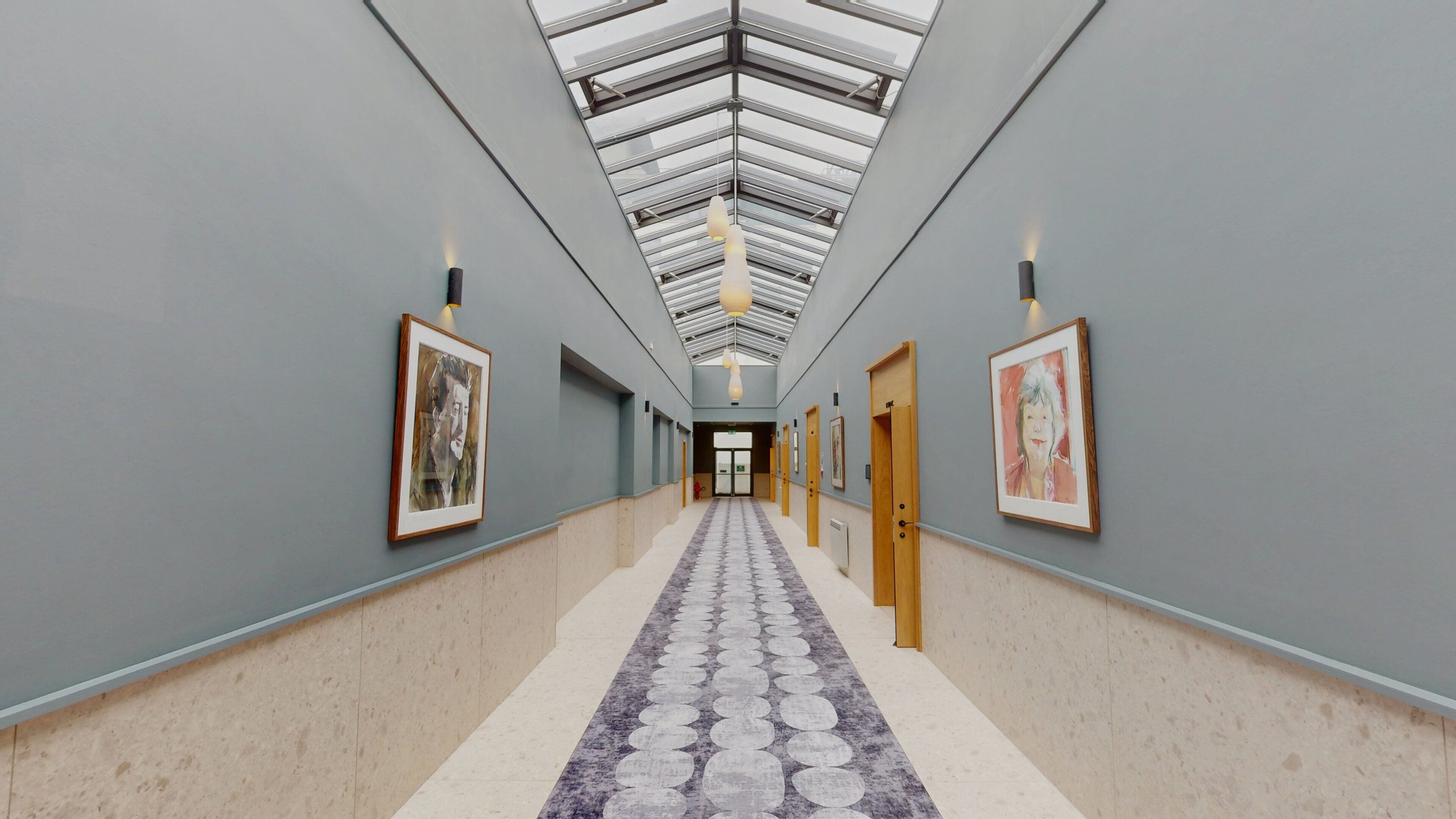 Un couloir doté d’une verrière, avec des œuvres d’art encadrées accrochées aux murs et un tapis à motifs.