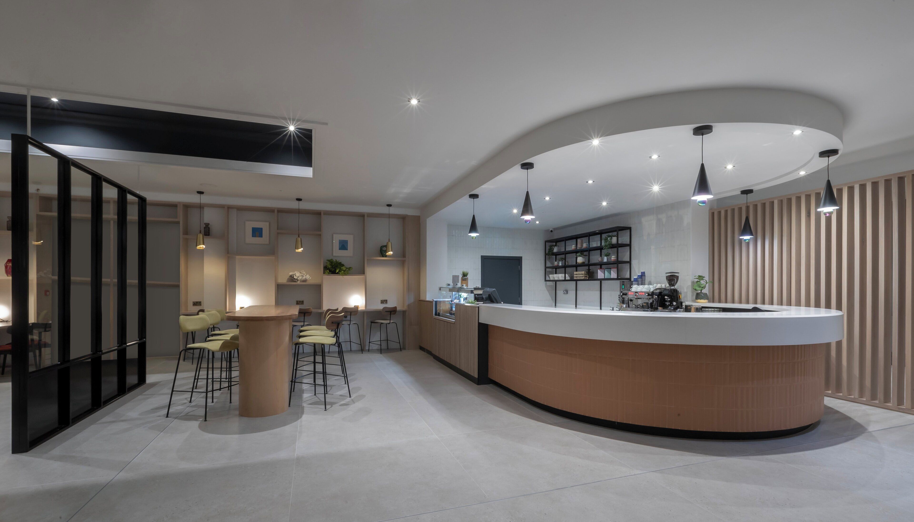Una cocina moderna con una isla curva, taburetes de bar, iluminación colgante y una cafetera integrada.