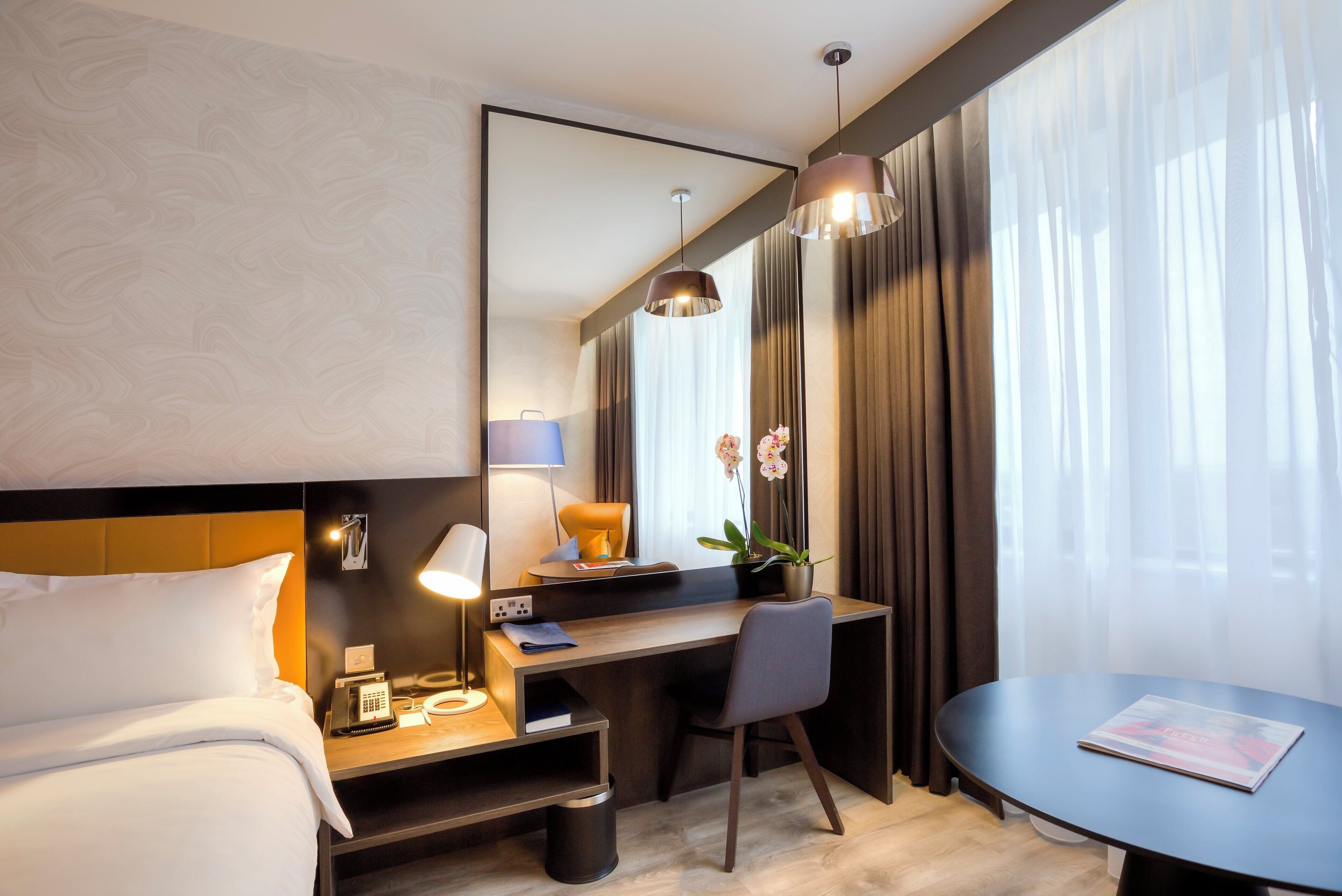 Quarto de hotel com cama, escrivaninha, cadeira e uma pequena mesa.
