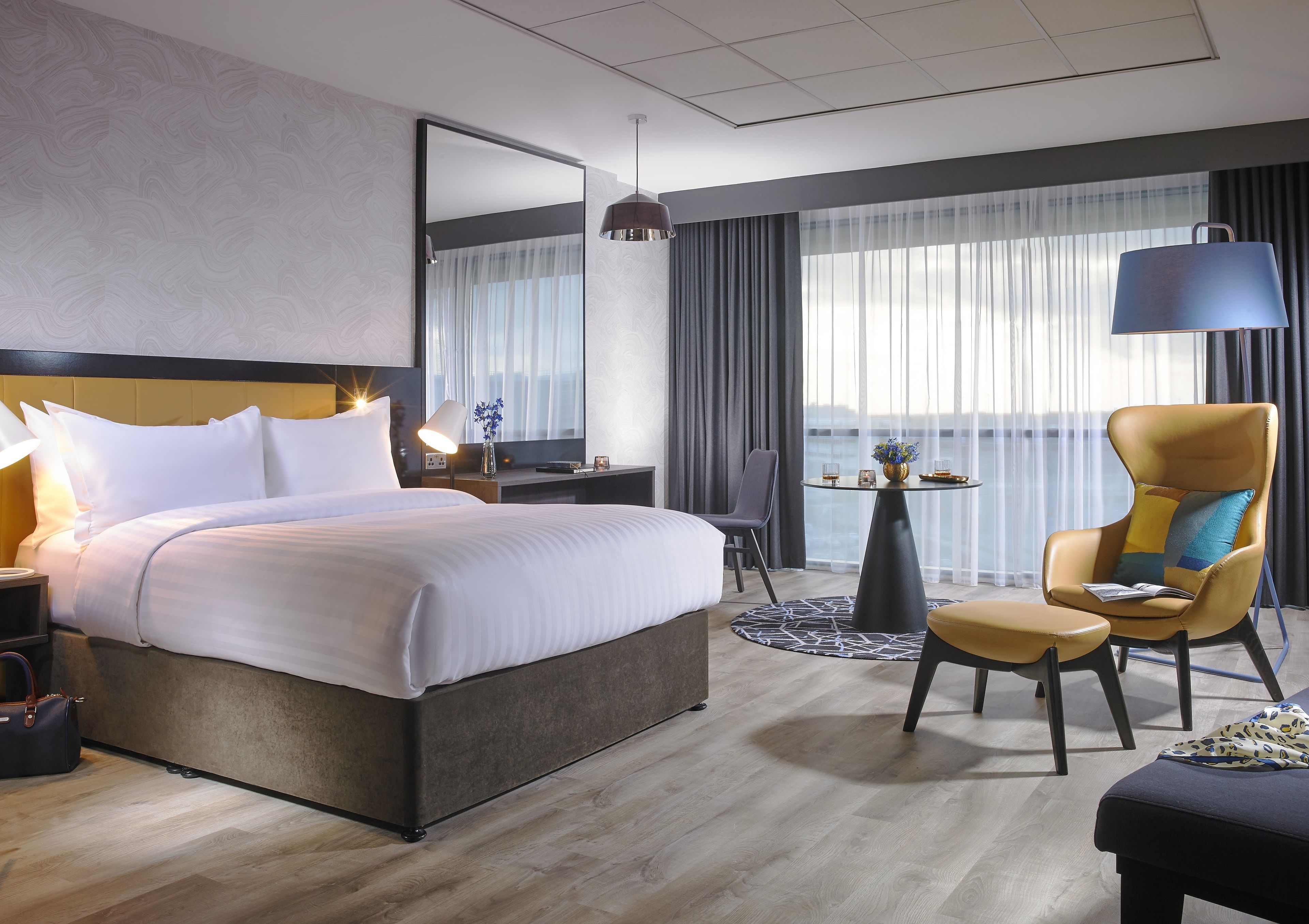 A hotel room with a large bed, a desk with a lamp, a chair, and a view of the outdoors.