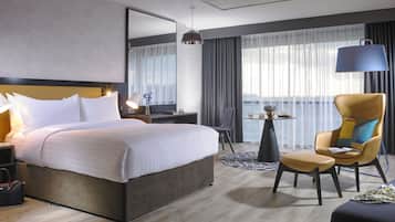 A hotel room with a large bed, a desk with a lamp, a chair, and a view of the outdoors.