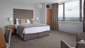 Moderni hotellihuone, jossa on suuri sänky, yöpöytä, tuoli ja näkymä lentokentälle.