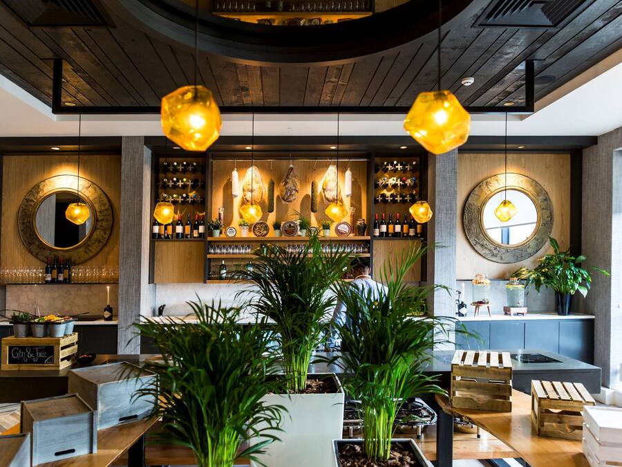 A modern bar area with wooden ceiling, hanging pendant lights, and a bartender at work.