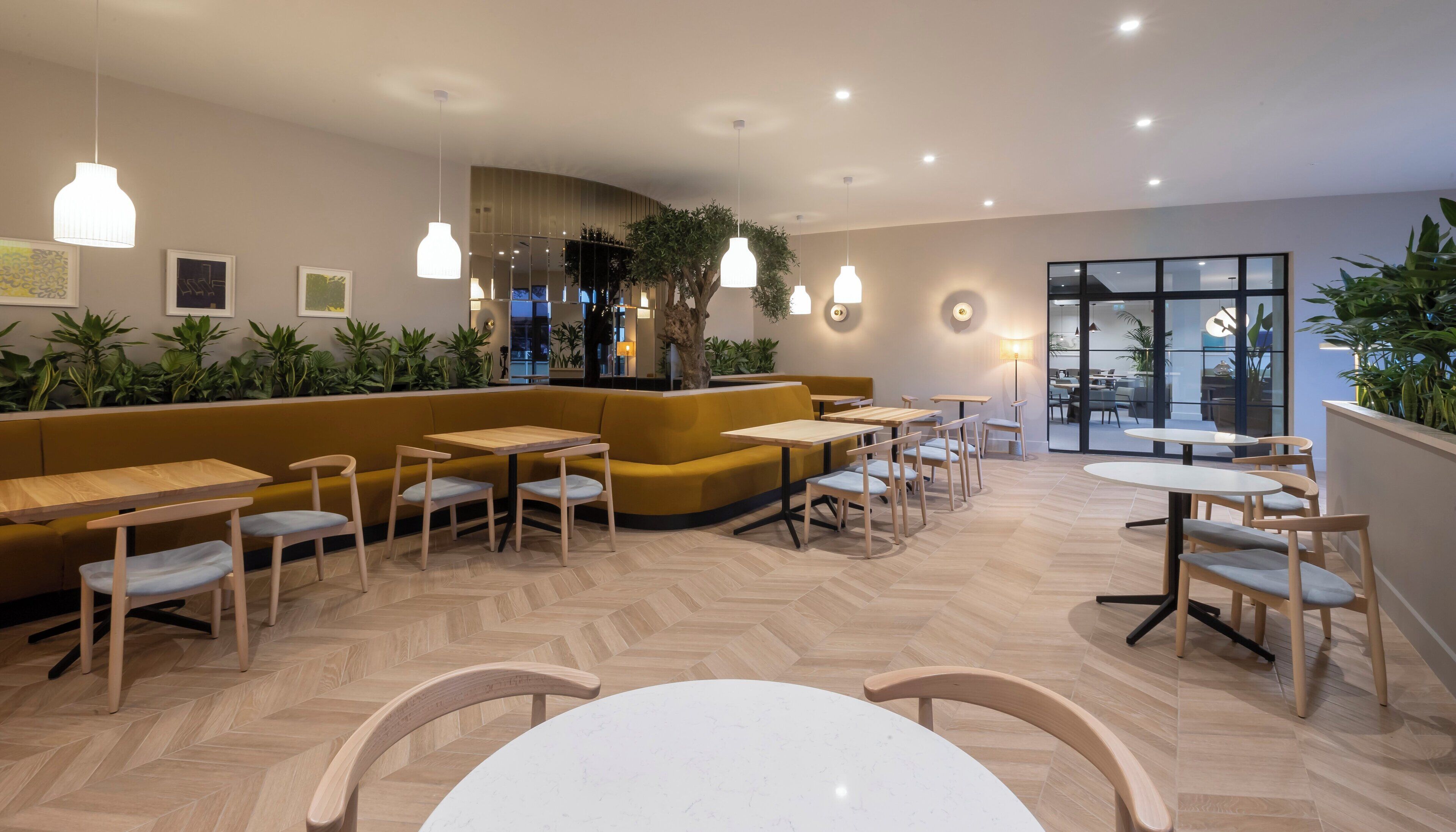 Interior moderno de una cafetería con mobiliario de madera, suelo de espiga y plantas de interior.