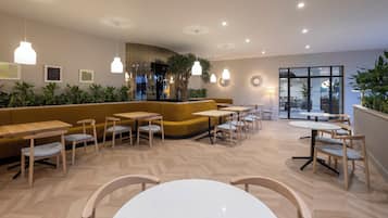 Interior moderno de una cafetería con mobiliario de madera, suelo de espiga y plantas de interior.