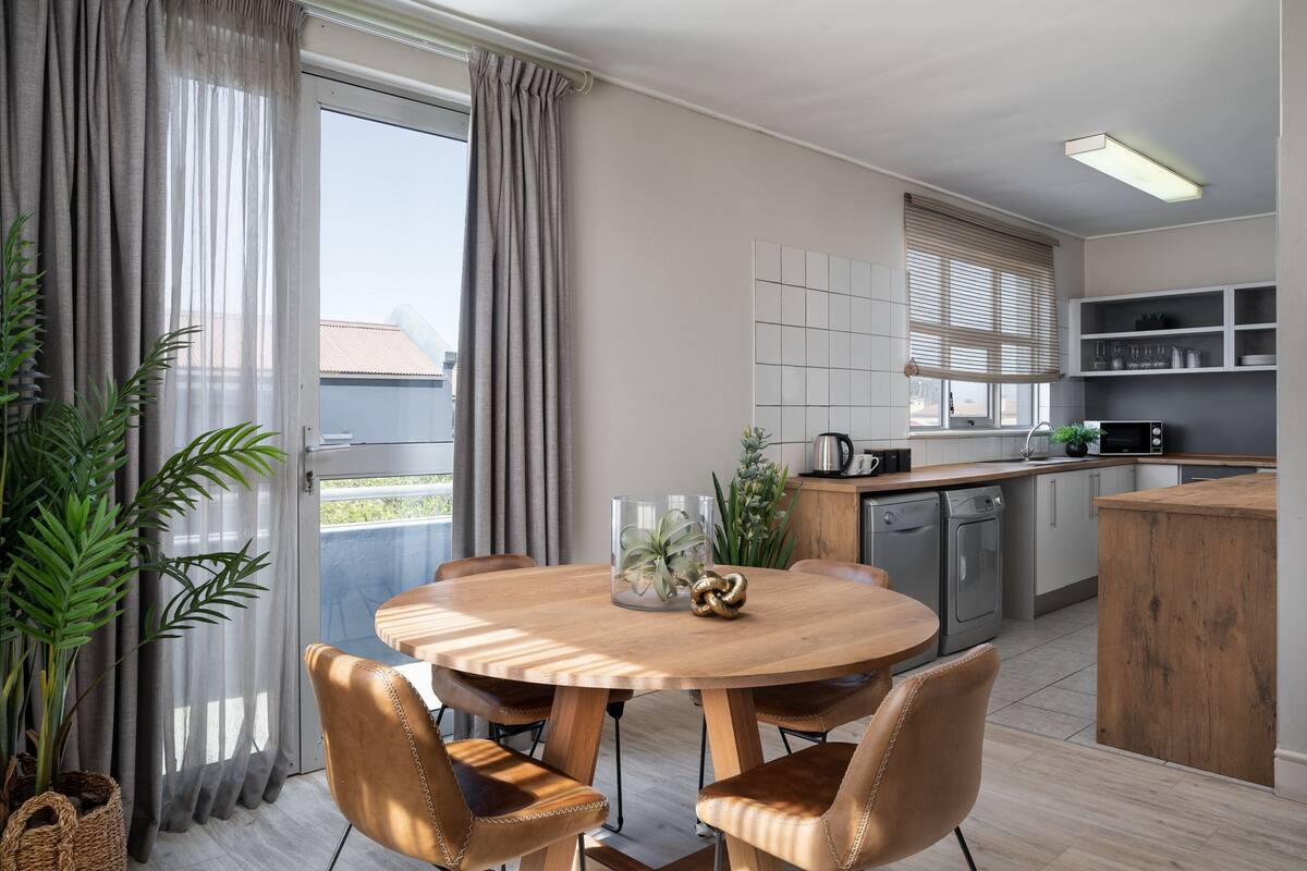 A modern kitchen with a wooden dining table, chairs, and a view of the outside.