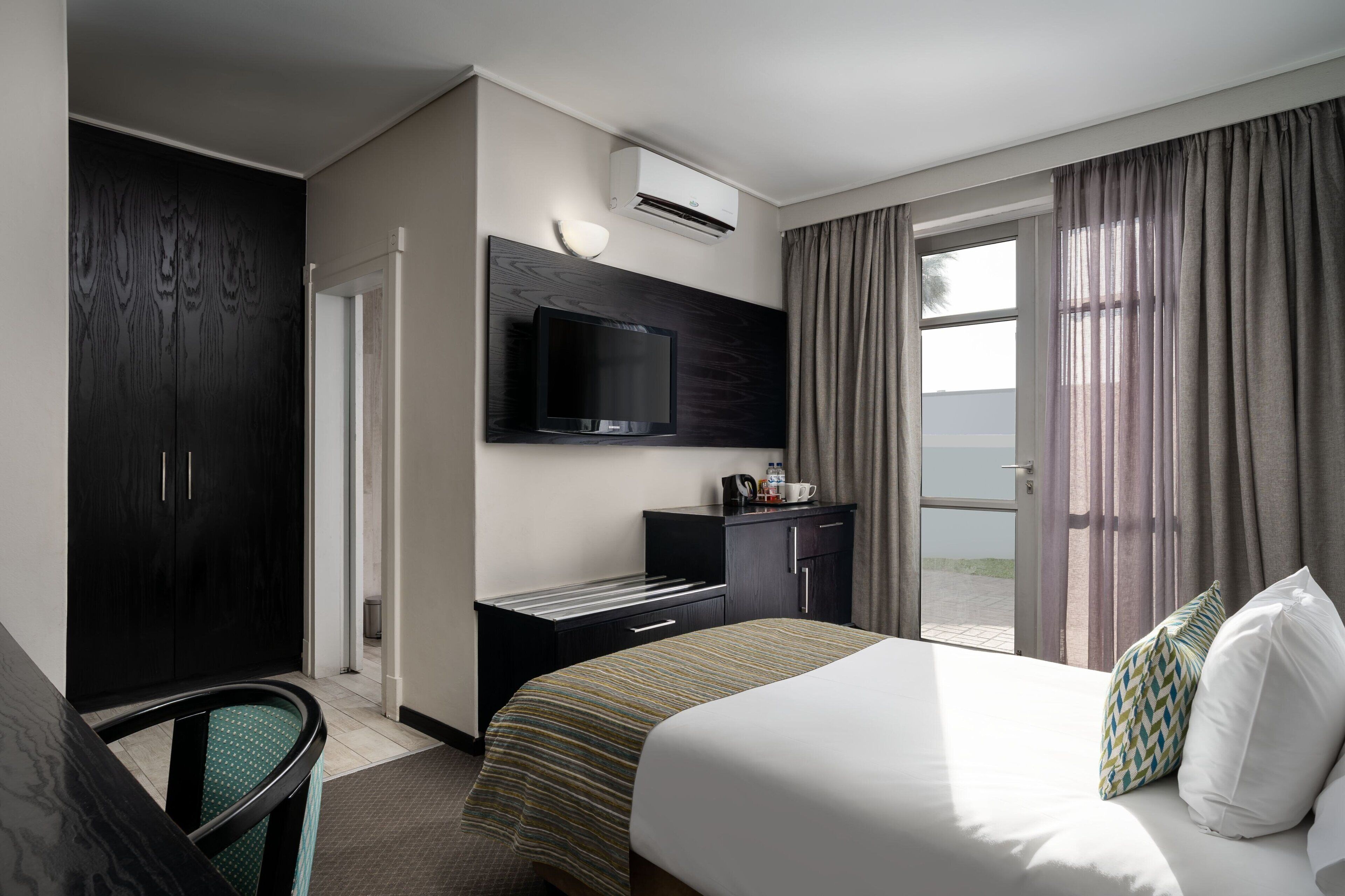 Quarto de hotel com cama, escrivaninha, televisão e janela com cortinas.