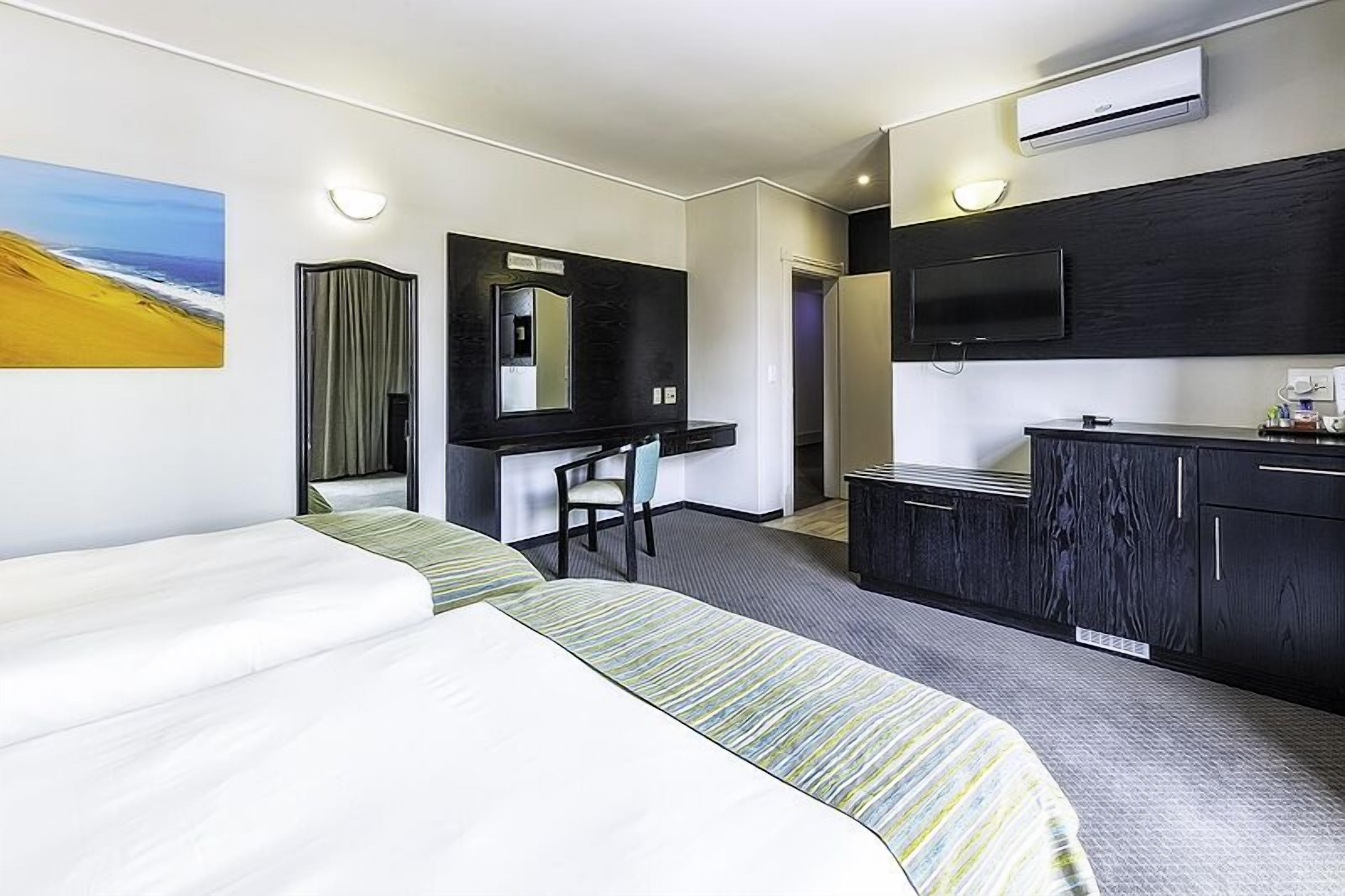 Una habitación de hotel con cama, escritorio, silla, televisor y minibar.