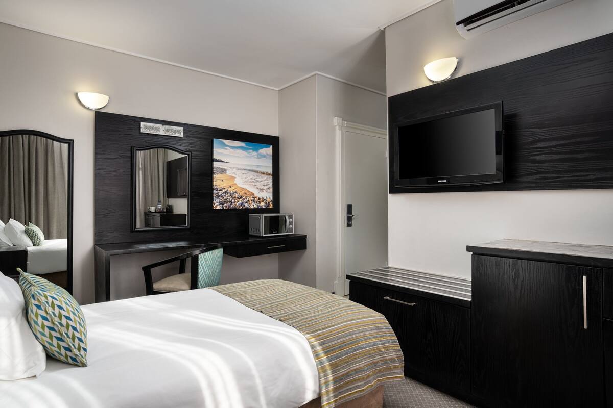 A modern hotel room with a bed, a desk, a flat-screen TV, and a large mirror.