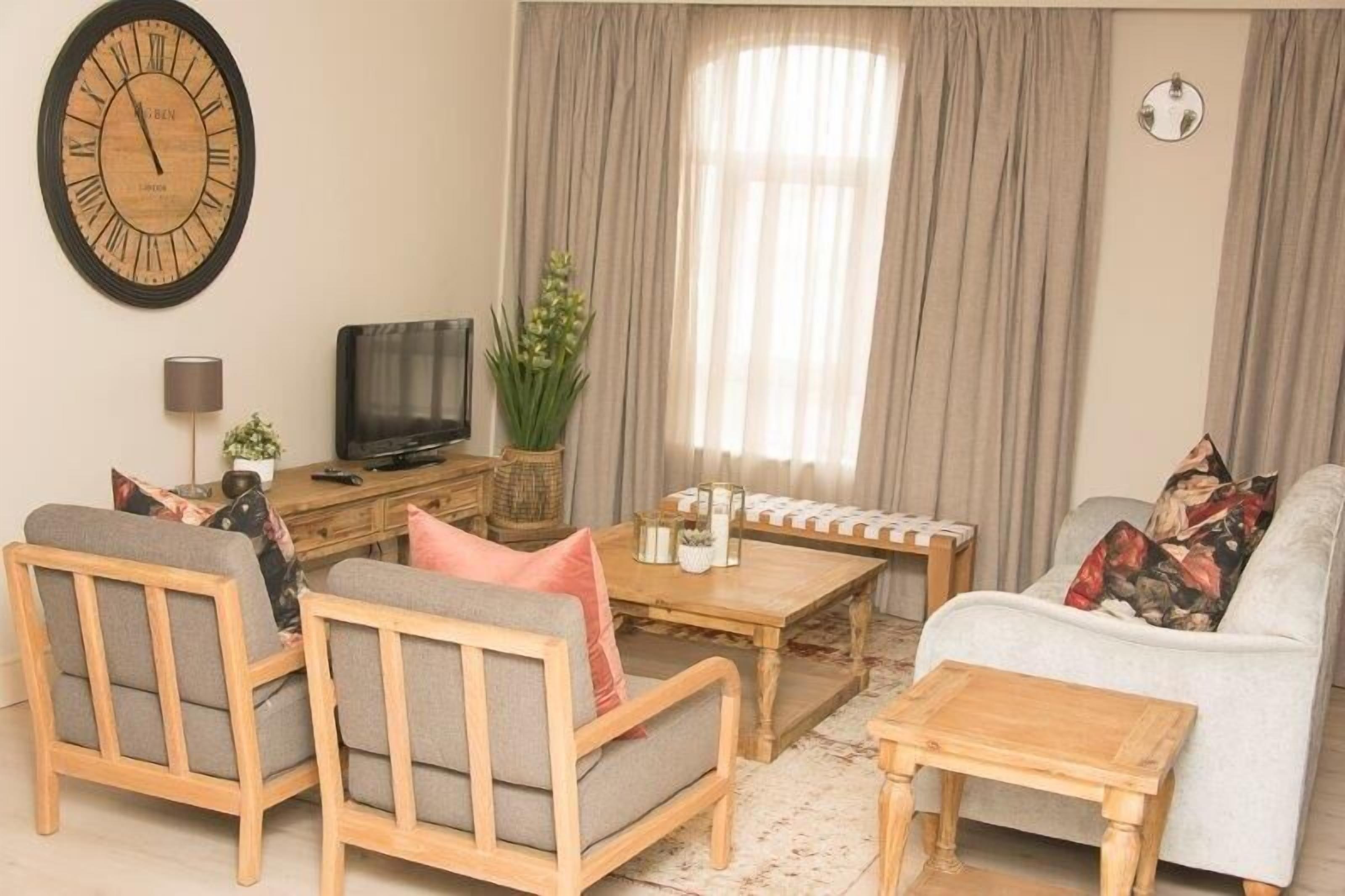 A living room with a wooden sofa, two armchairs, a coffee table, a television, and a large wall clock.