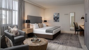 Una habitación de hotel moderna con una cama grande, una zona de estar con una mesa de centro y un escritorio con una silla.