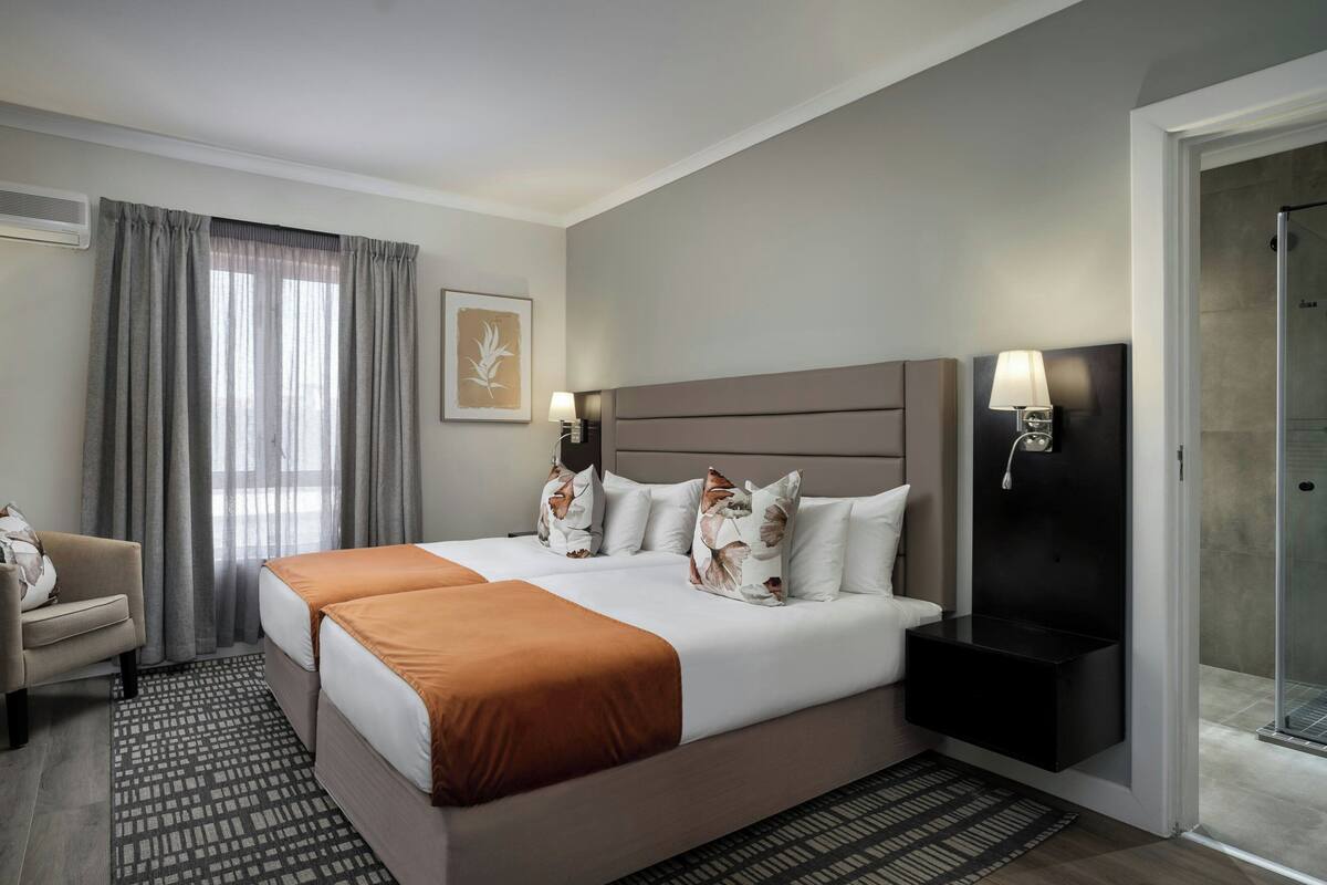 A hotel room with a large bed, a sofa, a desk, a lamp, and a shower area.