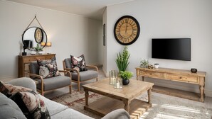 Una sala de estar moderna con un sofá, dos sillones, una mesa de centro, un televisor, un reloj de pared grande y una consola de madera.