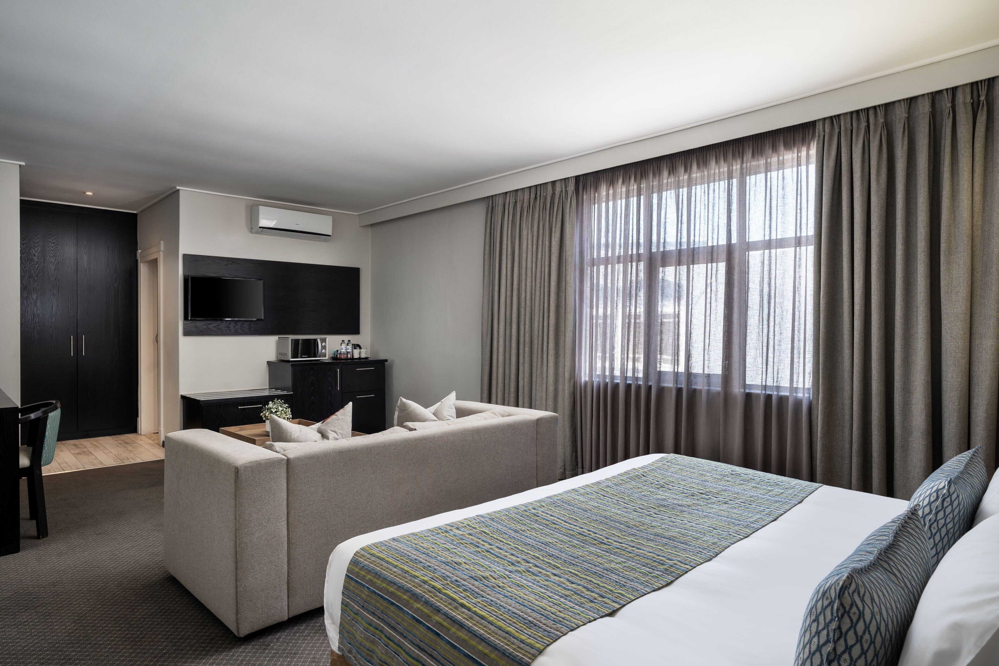 A hotel room with a bed, a sofa, a desk, and a TV.
