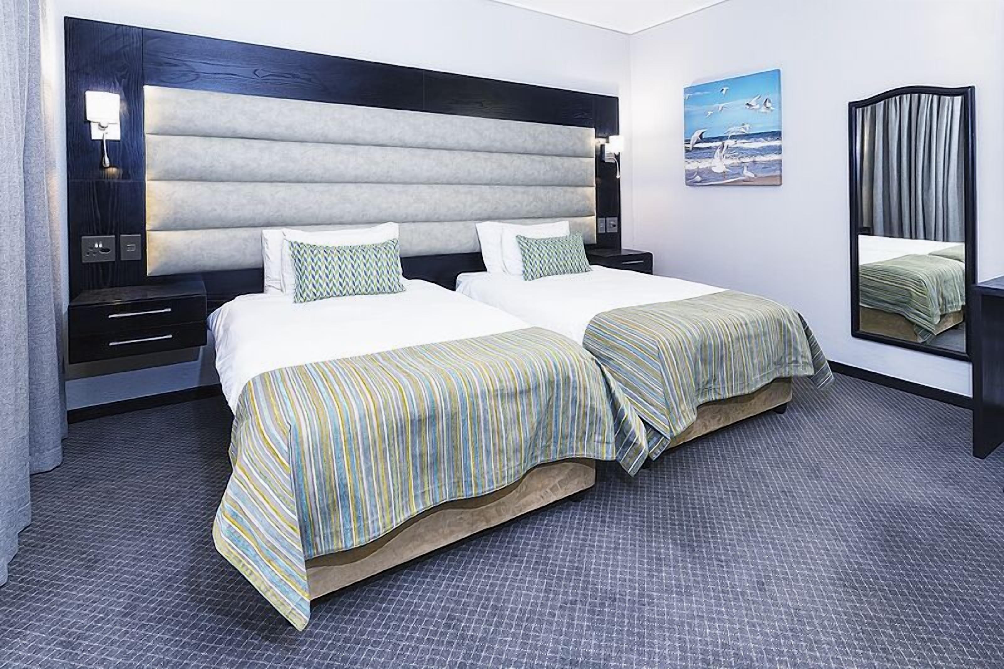 A double bed with striped bedding, a large headboard, bedside tables, and a nightstand.