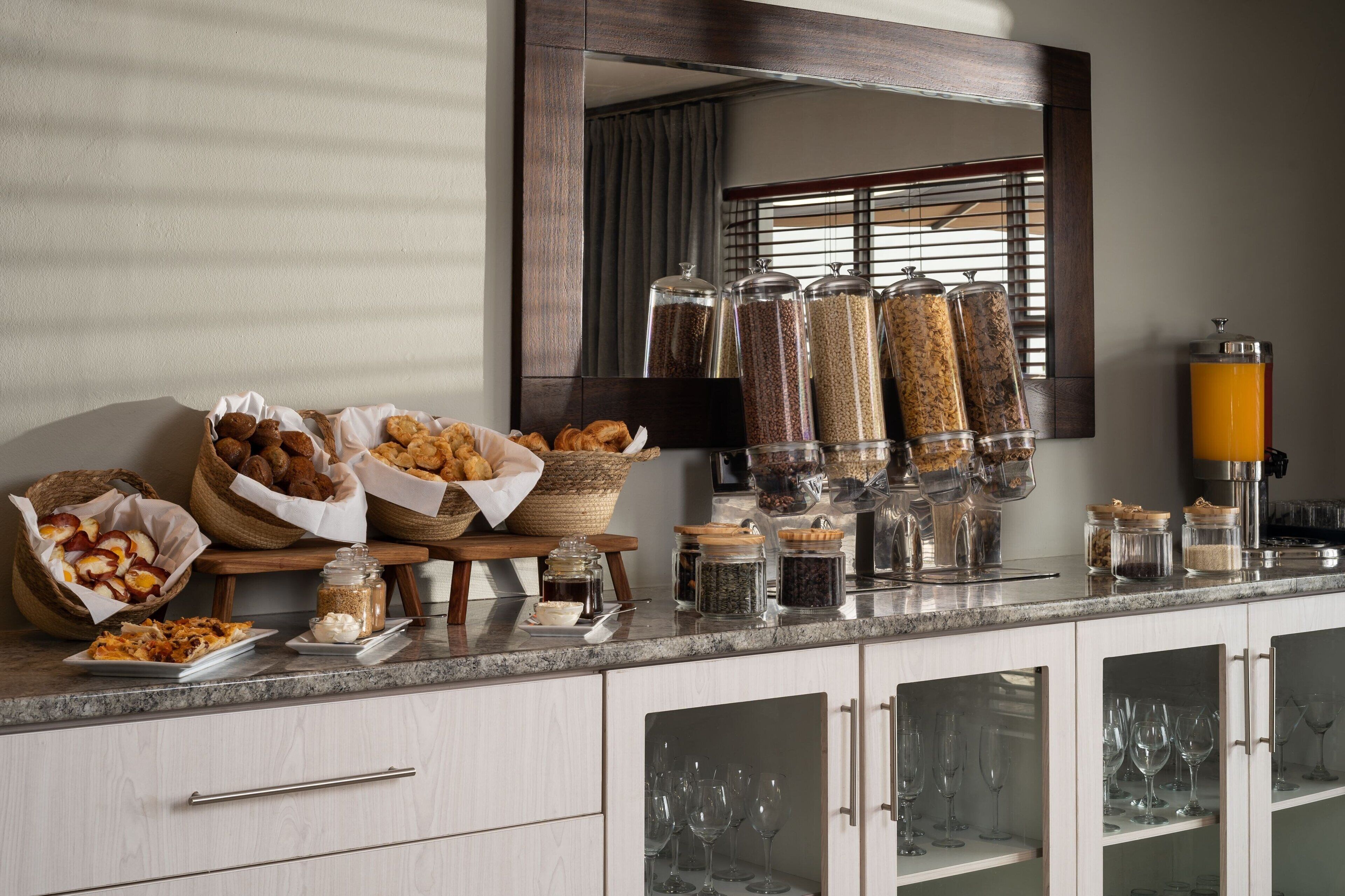 A breakfast buffet with various food items and beverages, including jars of cereal and a coffee machine.