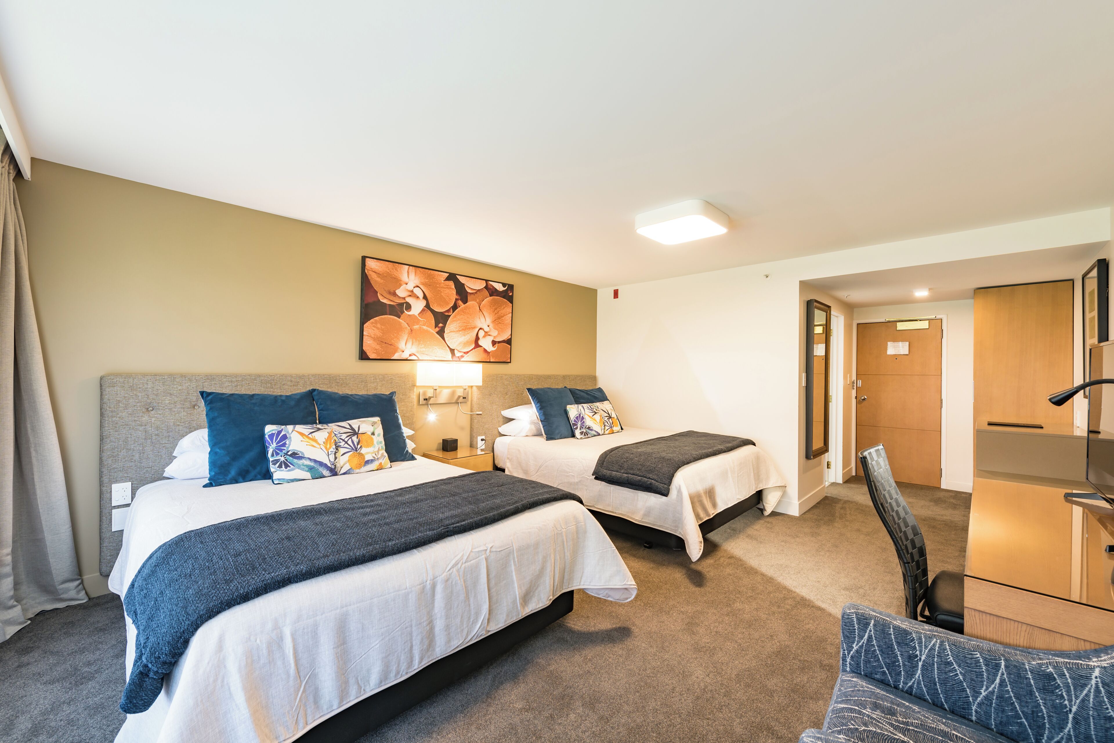 A hotel room with two beds, a desk, a chair, and a painting on the wall.