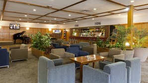 Um saguão de hotel com áreas de estar, um piano, um bar e uma tela de televisão.