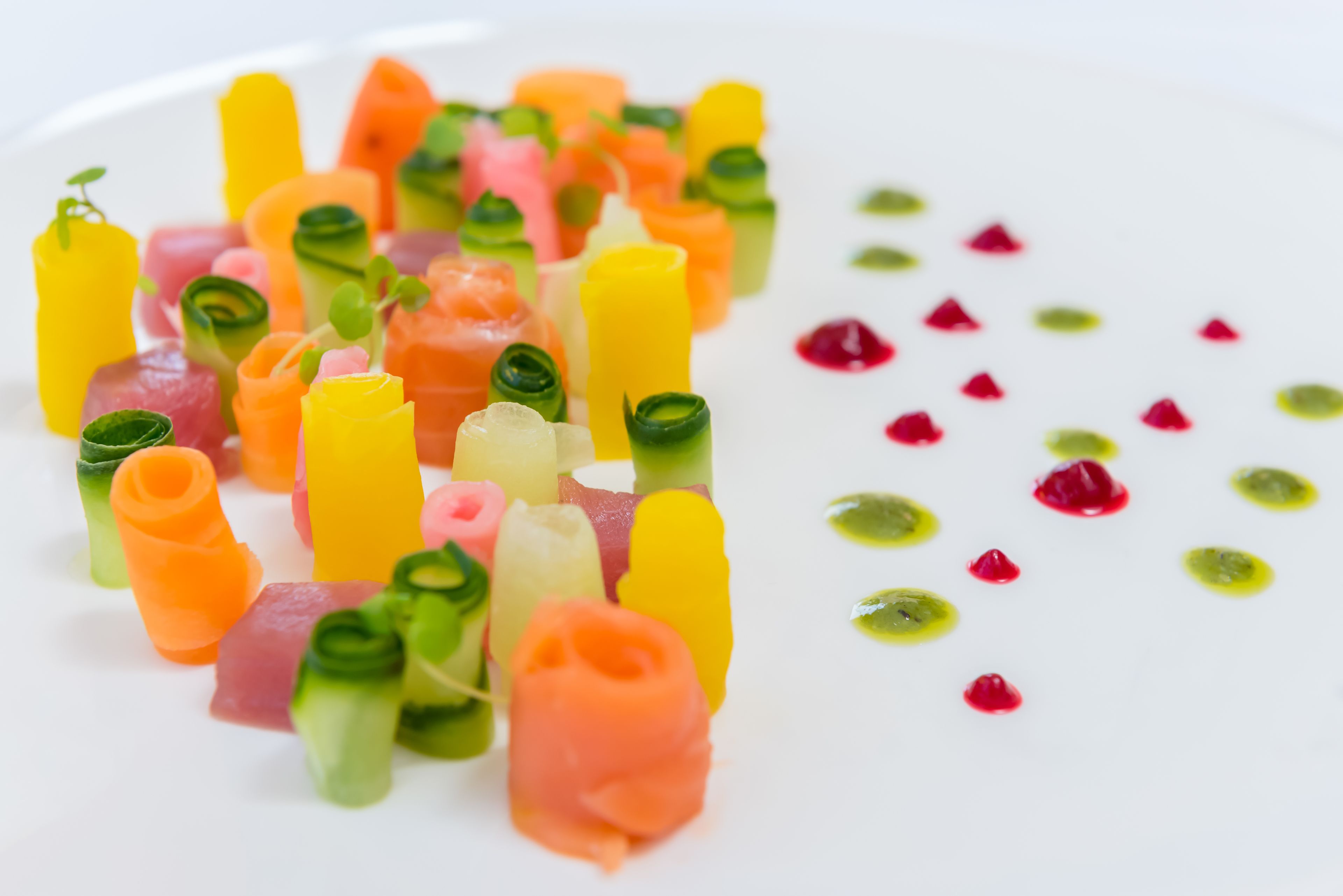 A white plate with colorful food items, including pink, yellow, and green elements, and small red dots.