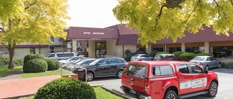 A hotel reception with a red car parked in front, surrounded by neatly trimmed bushes and trees.