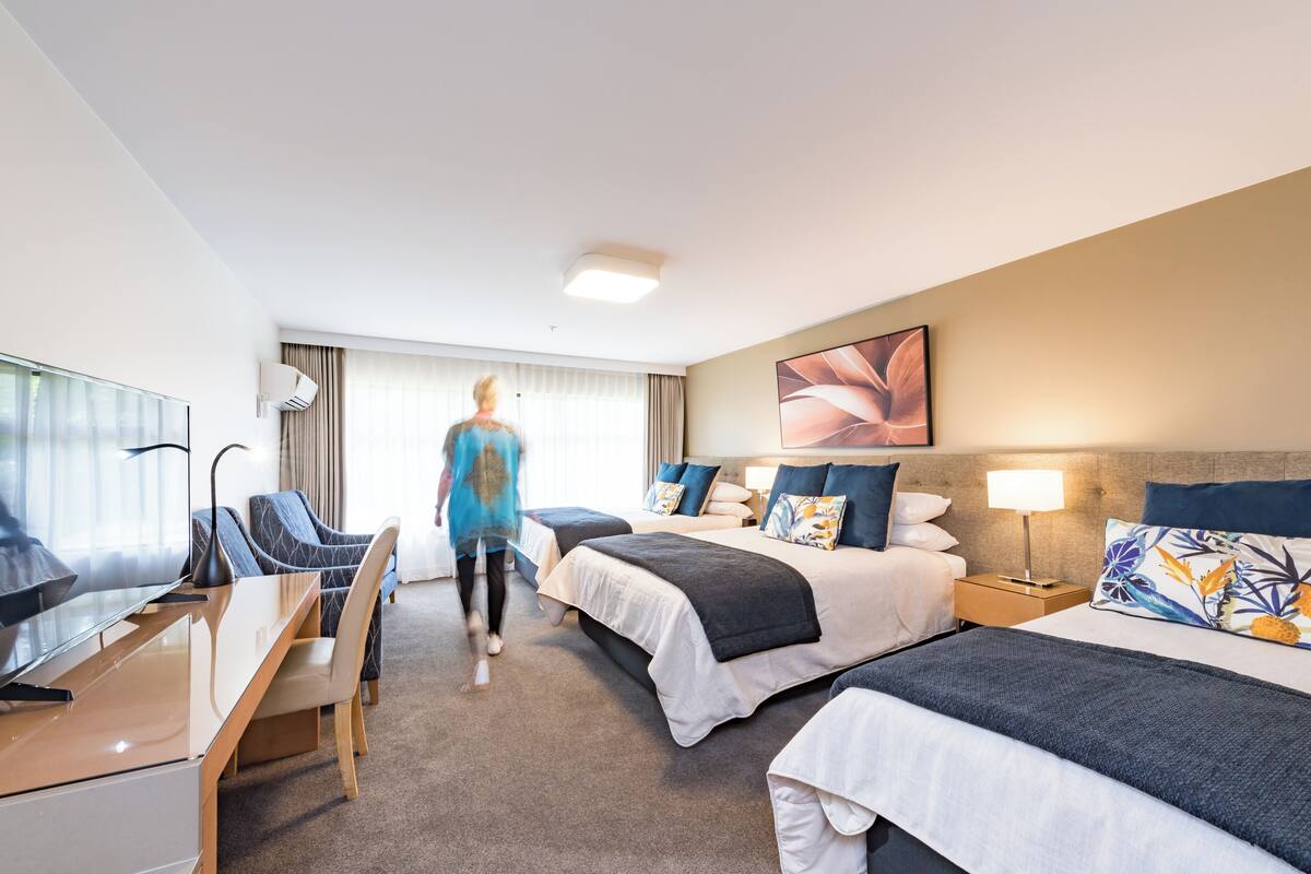 Une chambre d’hôtel avec deux lits, un bureau, une télévision et une grande fenêtre avec des rideaux.