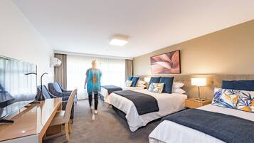 A hotel room with two beds, a desk, a TV, and a large window with curtains.