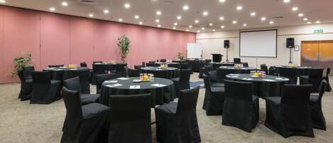 A conference room with round tables, black chairs, and a projector screen.