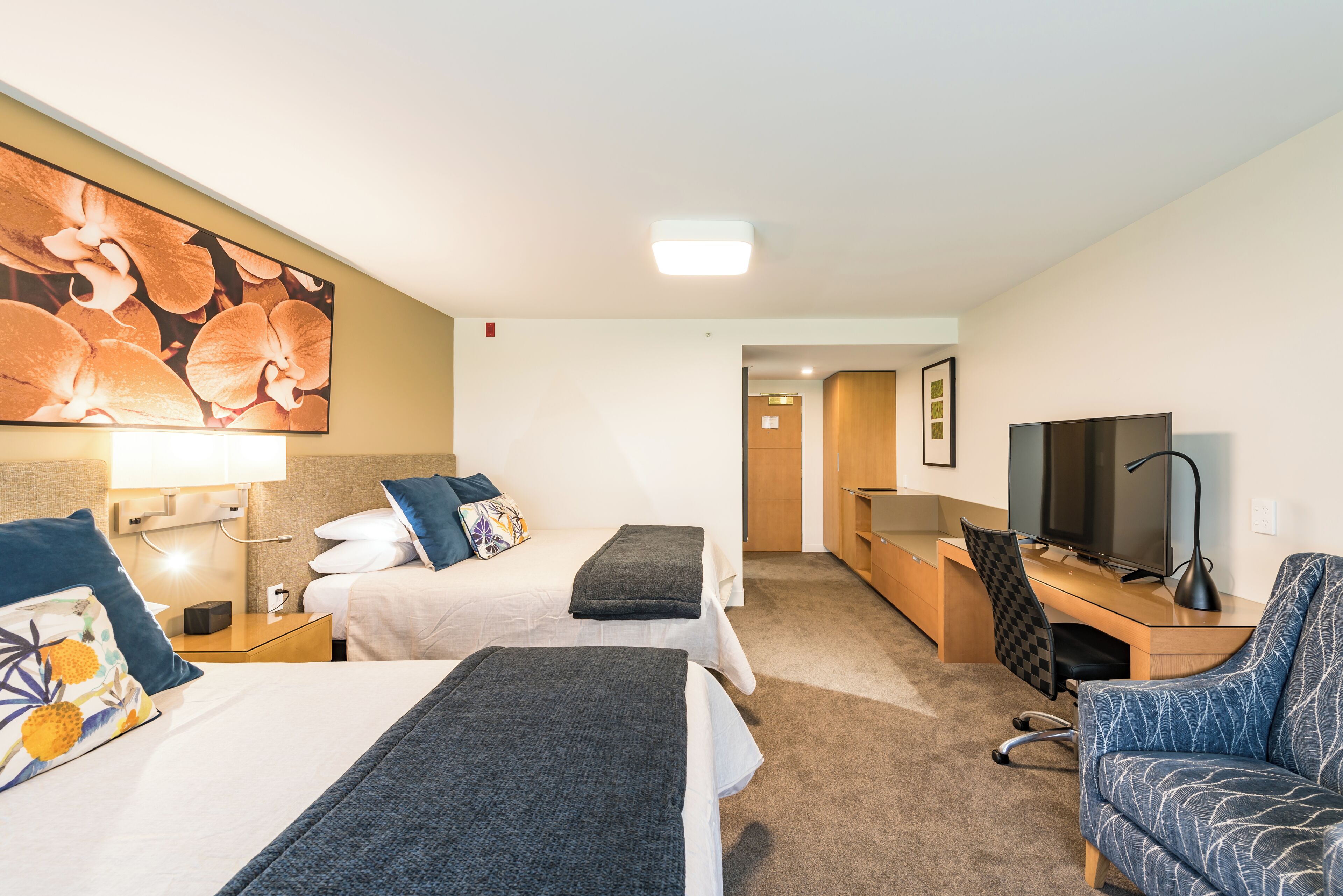 A hotel room with two beds, a desk with a computer, a TV, and a chair.