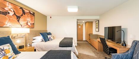 A hotel room with two beds, a desk with a computer, a TV, and a chair.
