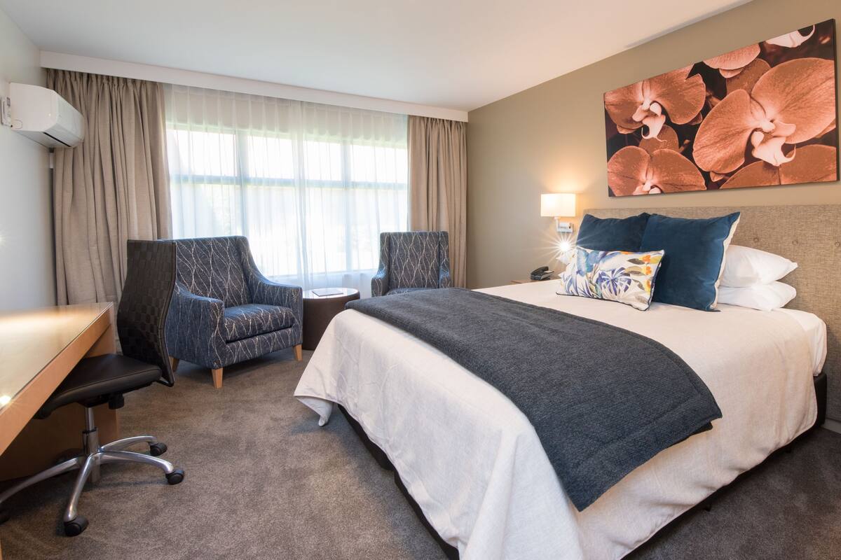 Une chambre d’hôtel avec un grand lit, deux fauteuils, un bureau et une lampe fixée au mur.
