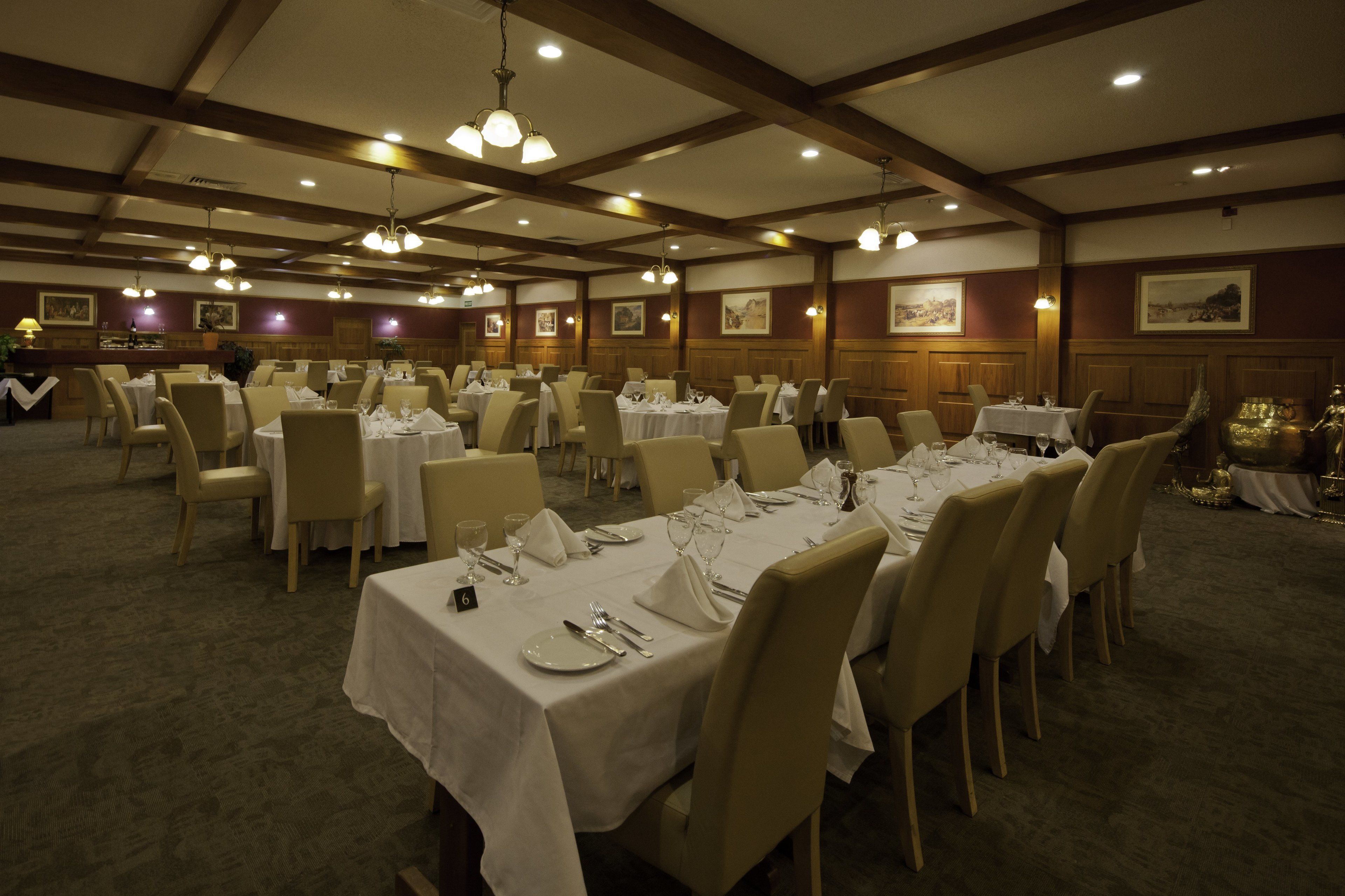 A banquet hall with multiple tables set for dining, featuring a high ceiling with wooden beams and chandeliers.