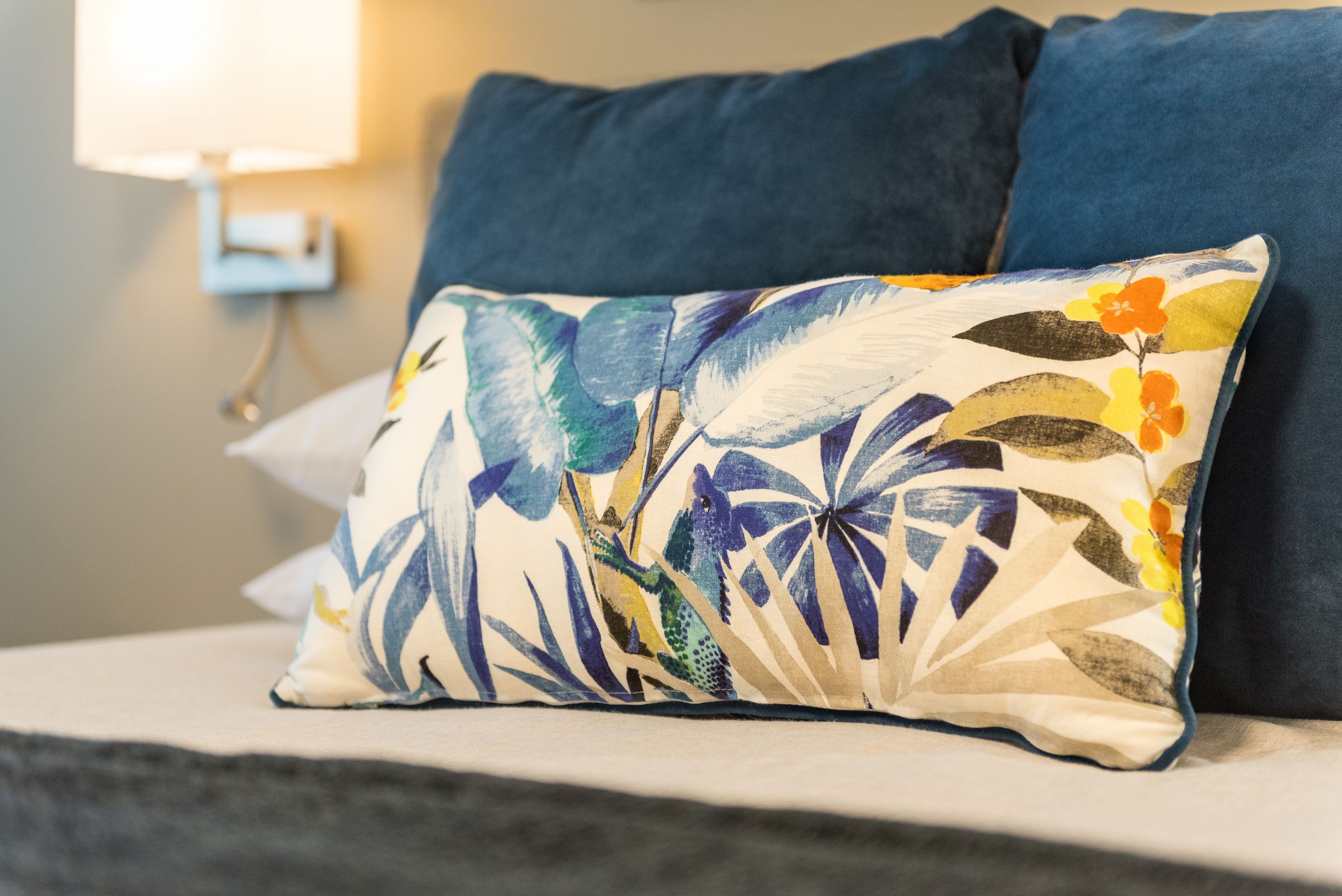 Una cama con un cojín estampado de flores y un cojín azul oscuro.