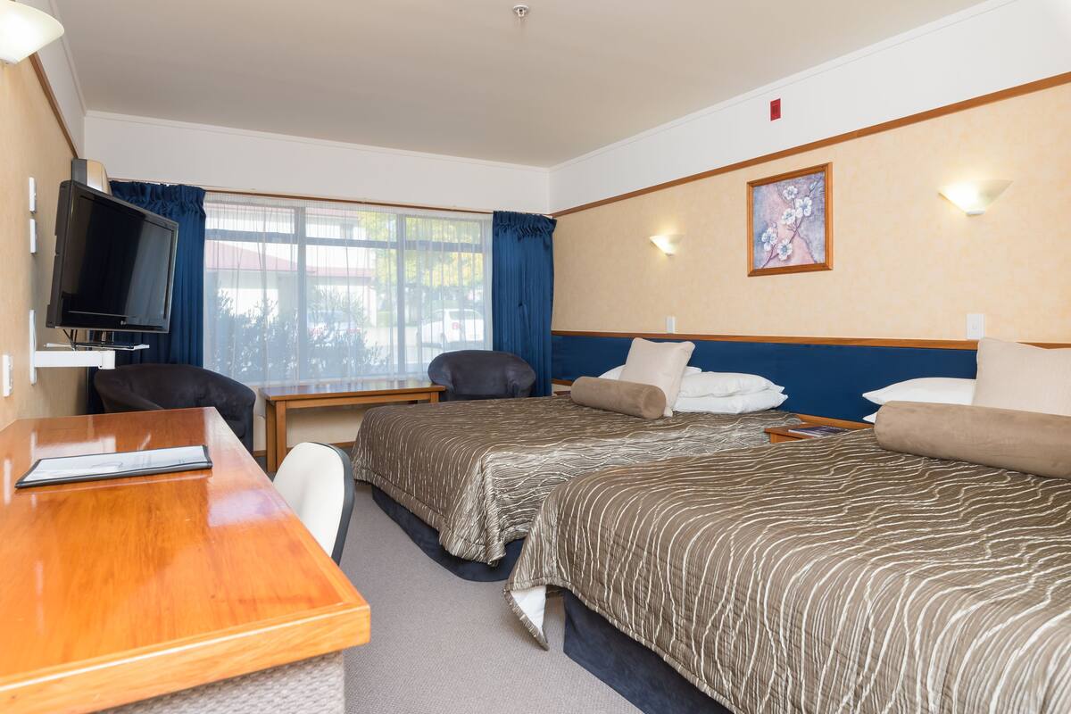 Une chambre d’hôtel avec deux lits, un bureau, une télévision et une fenêtre avec des rideaux.