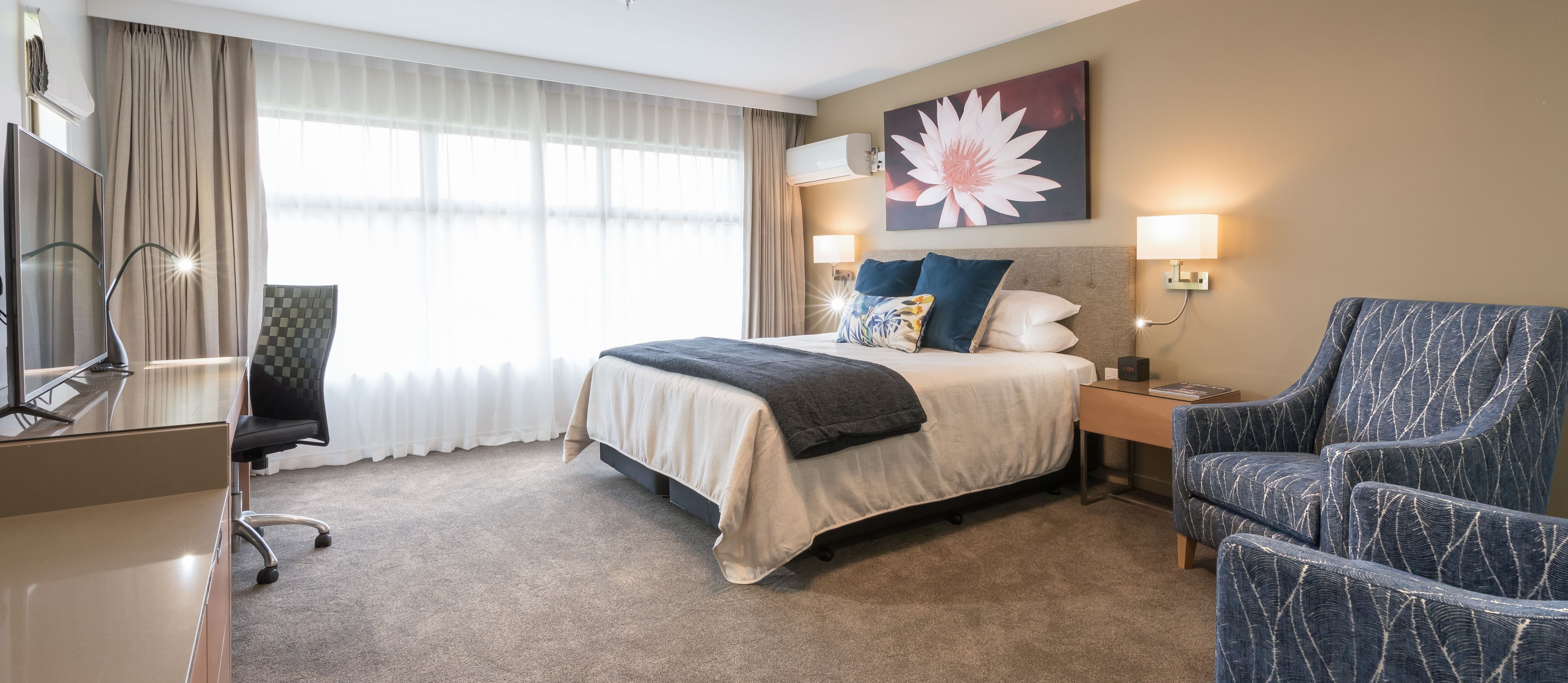 A hotel room with a bed, a desk, a chair, and a large window with curtains.