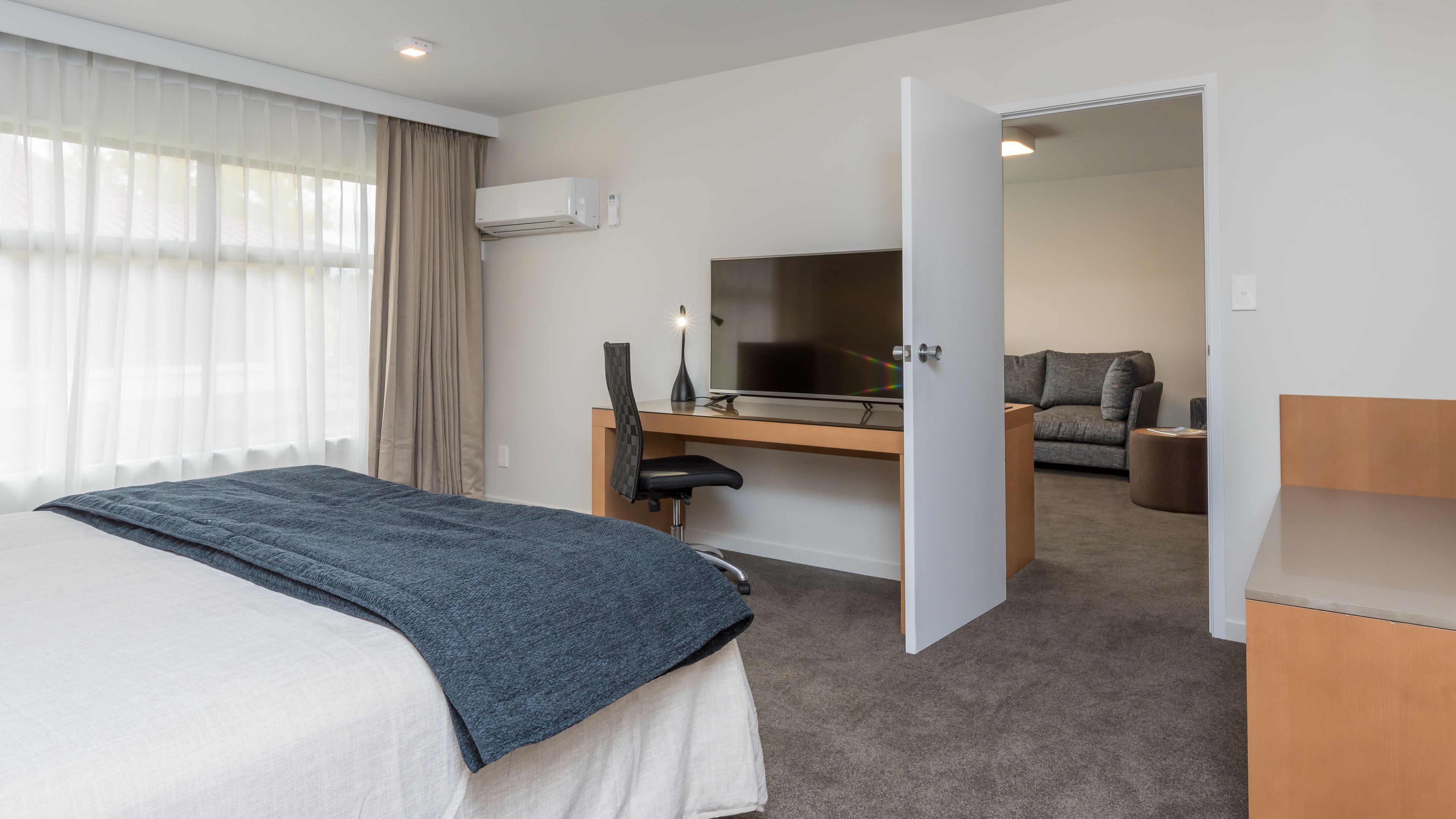 A hotel room with a bed, a desk with a computer, a TV, and a sofa in the adjacent room.