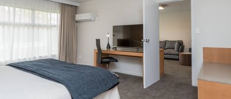 A hotel room with a bed, a desk with a computer, a TV, and a sofa in the adjacent room.