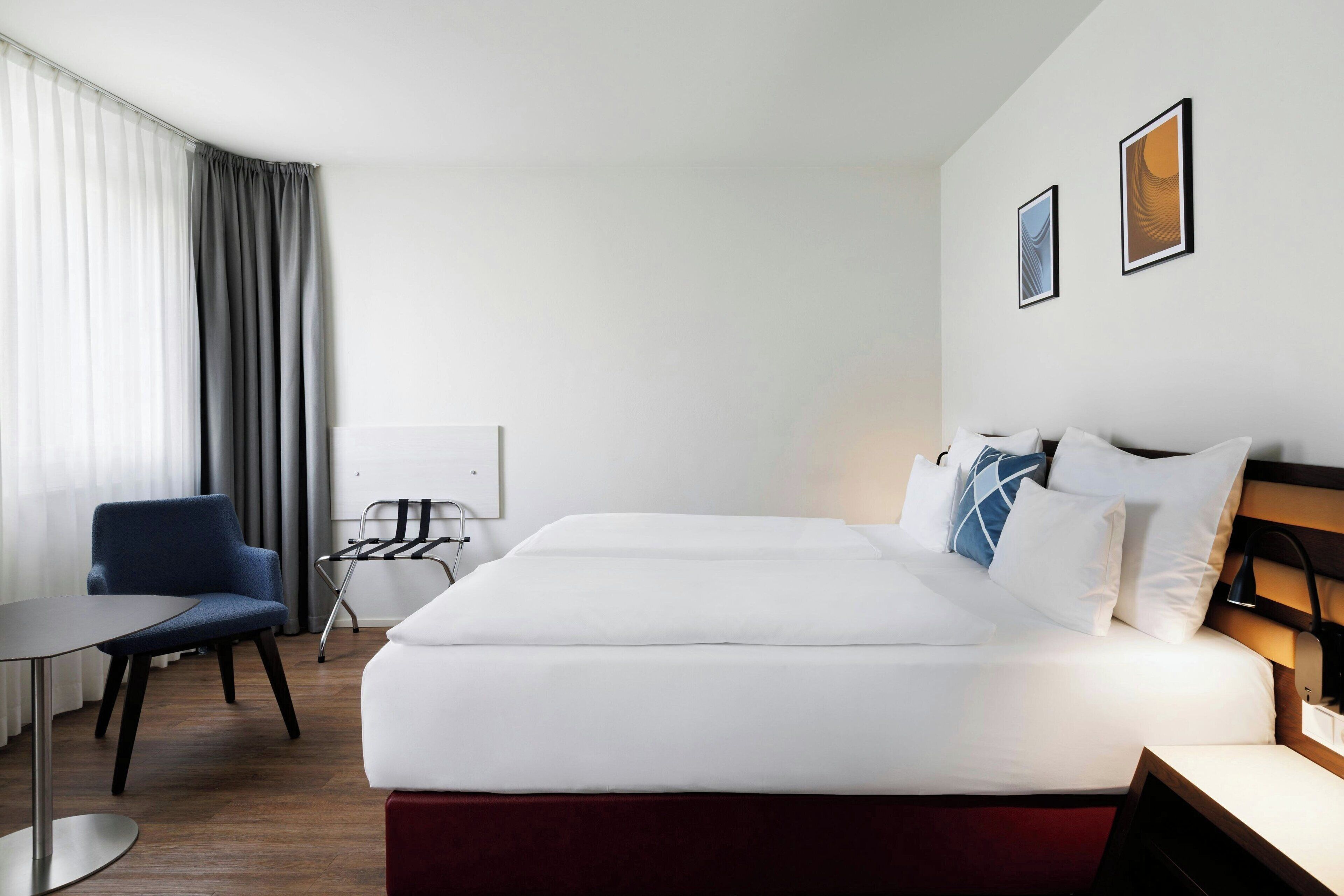 A hotel room with a large bed, a desk, a chair, and a window with curtains.