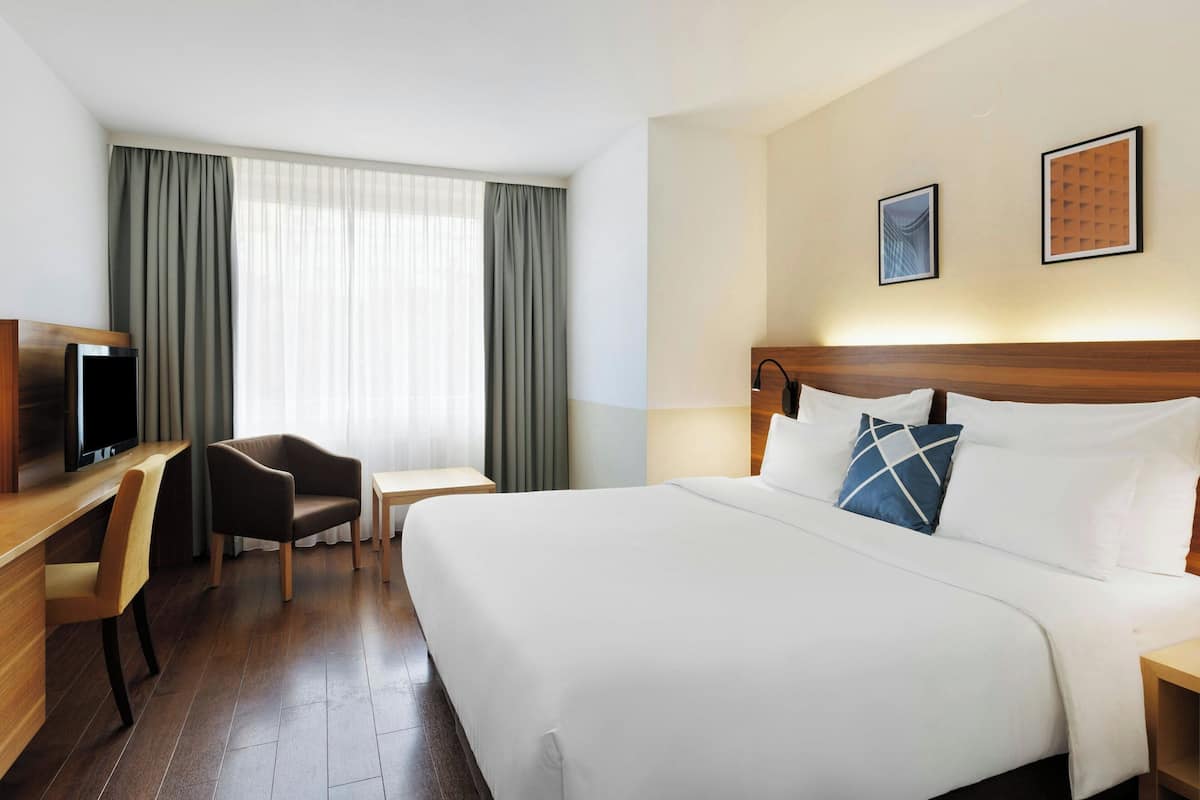Una habitación de hotel con una cama grande, un escritorio con silla, televisión y ventana con cortinas.