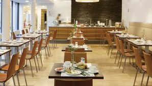 Een moderne eetruimte met lange tafels, stoelen en een decoratieve plant in het midden.