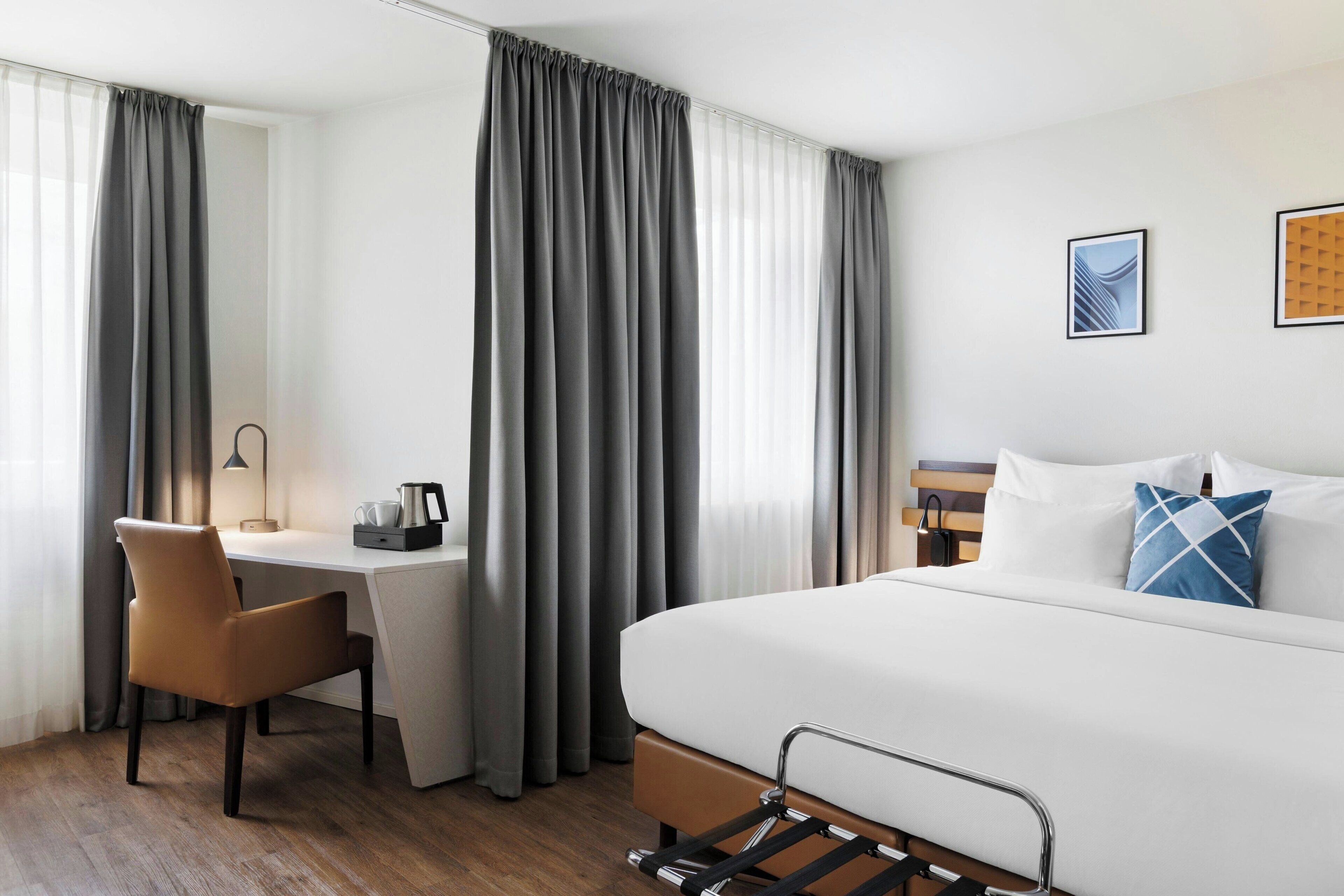 Quarto de hotel com cama, escrivaninha, cadeira e cortinas.