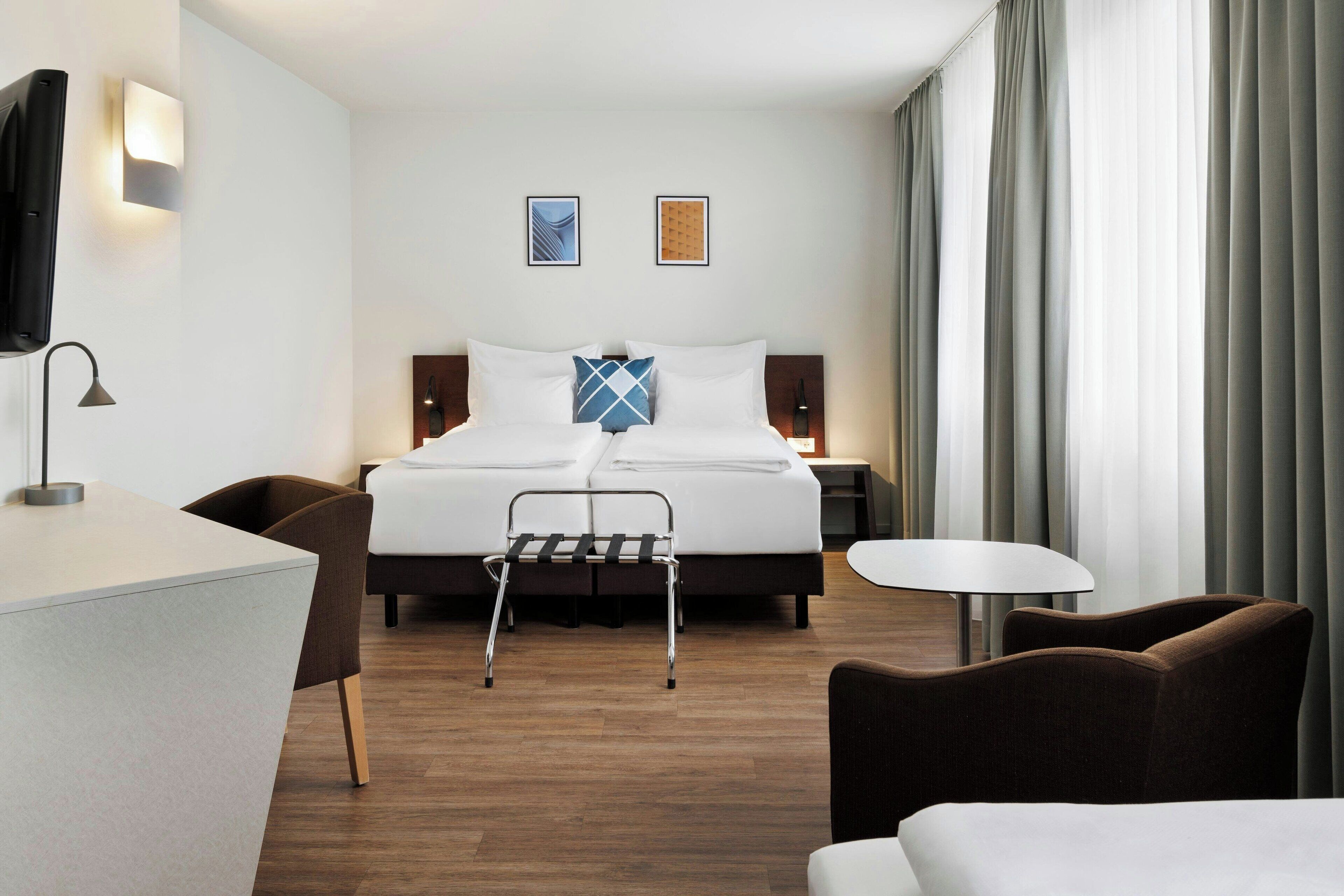 Une chambre d’hôtel moderne équipée d’un lit, de tables de chevet, d’un bureau, d’une chaise, d’une petite table et d’un téléviseur.