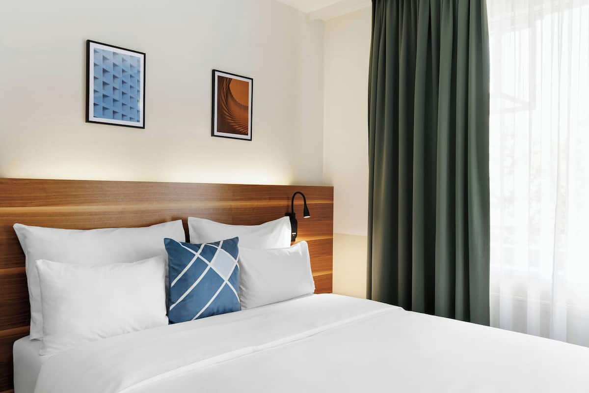 Una habitación de hotel con cabecera de madera, ropa de cama blanca y dos cuadros en la pared.