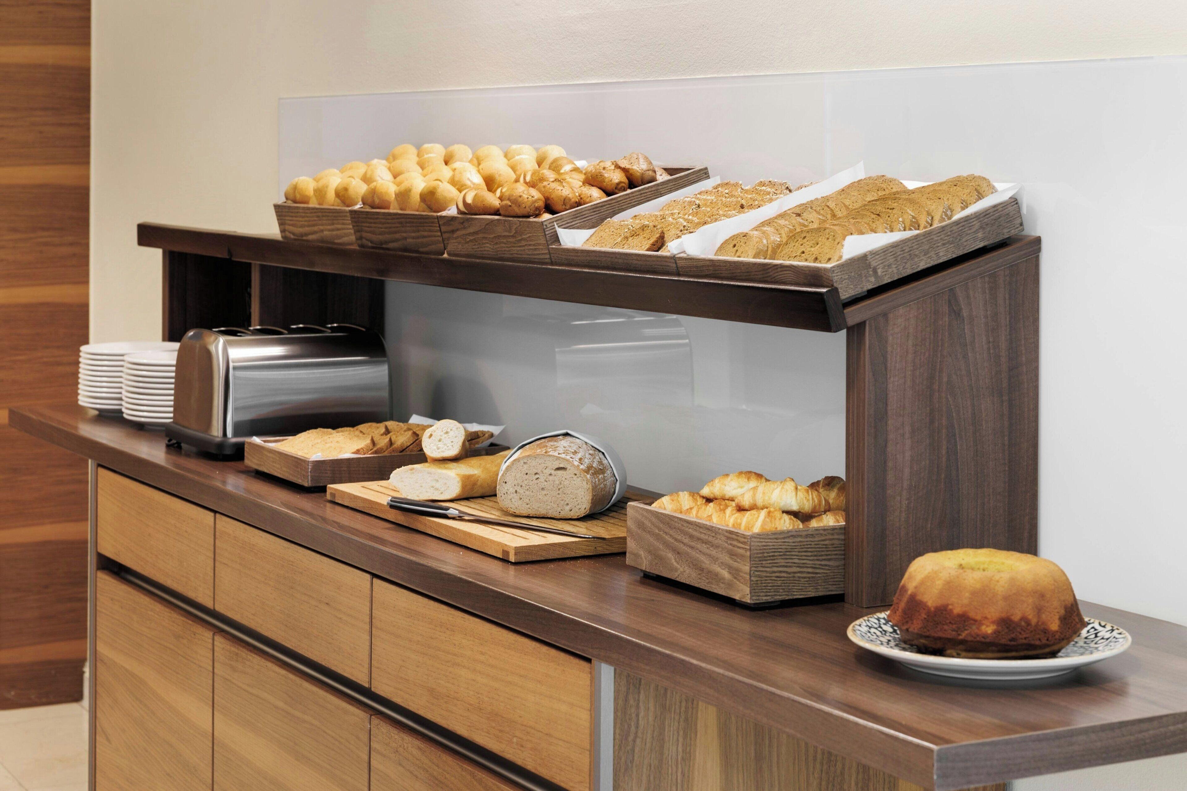 Un buffet proposant une variété de pains et de viennoiseries, une trancheuse à pain et un plateau de service.