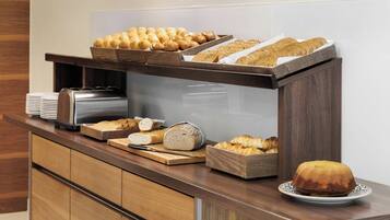 Un buffet proposant une variété de pains et de viennoiseries, une trancheuse à pain et un plateau de service.